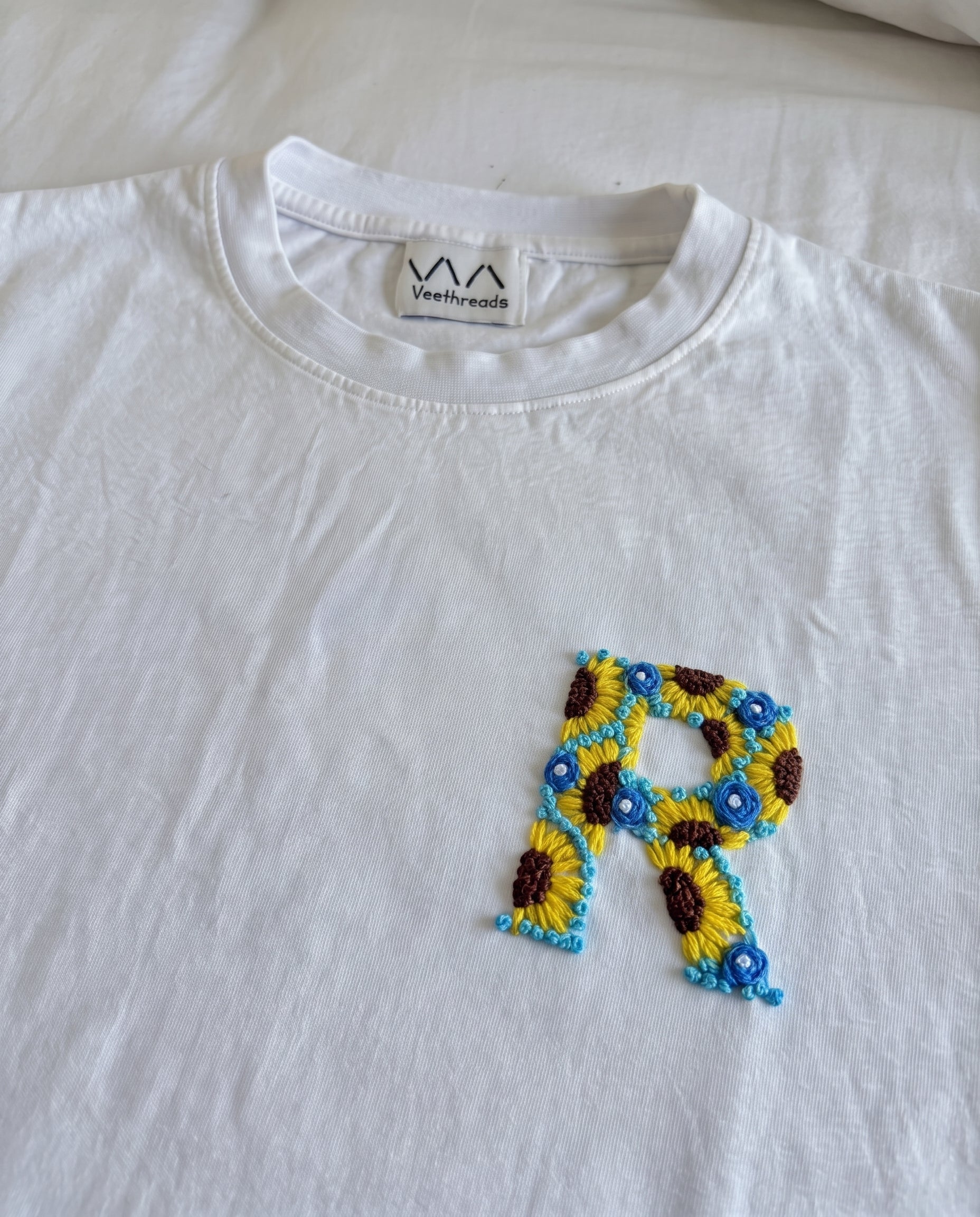 Hand-embroidered floral initial, sunflowers and blue flowers, on a white cotton tee by Vee Threads