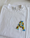 White cotton tee with an initial hand-embroidered as sunflowers and small blue flowers, by Vee Threads