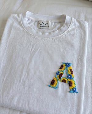 White cotton tee with an initial hand-embroidered as sunflowers and small blue flowers, by Vee Threads