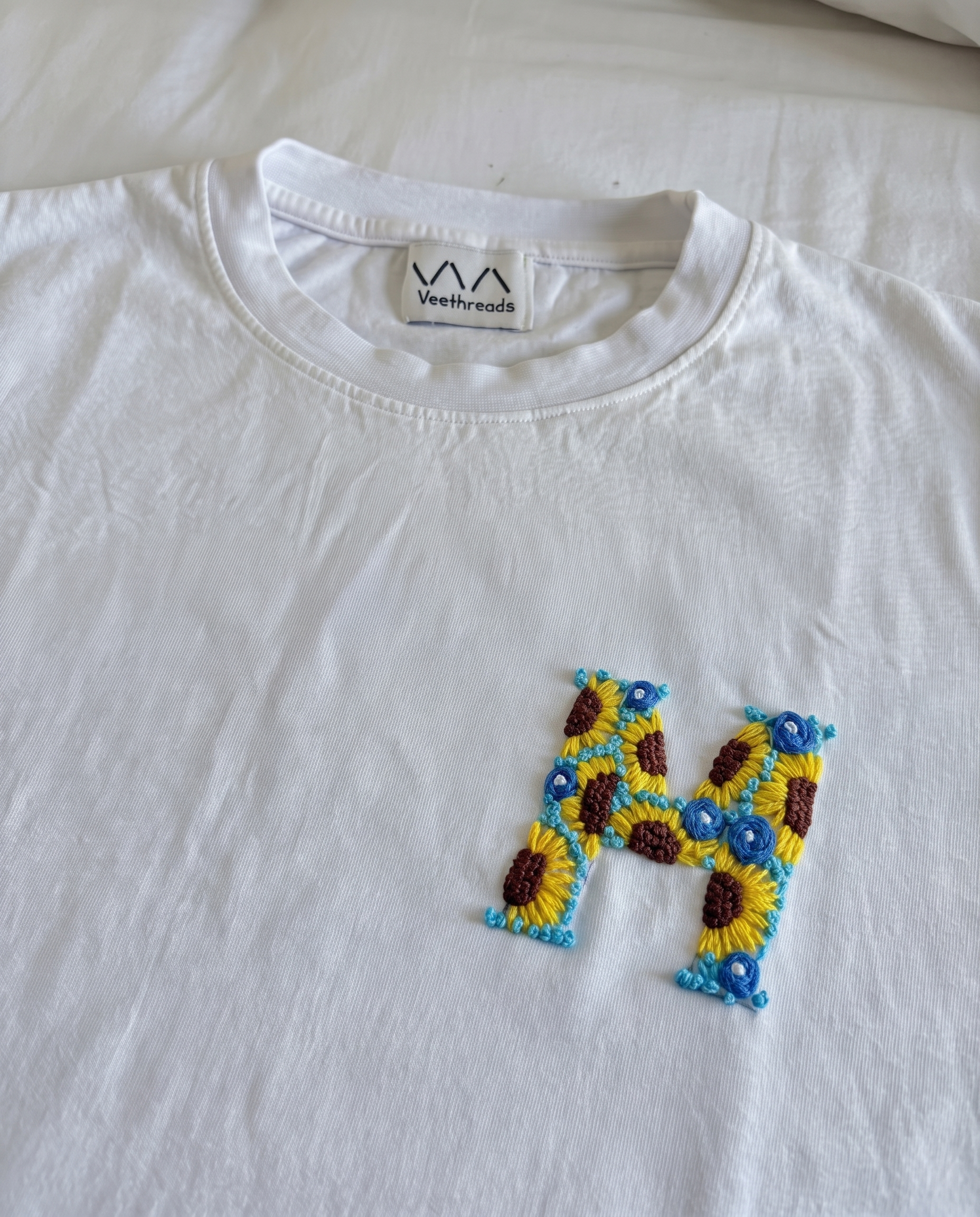 Sunflower and blue-flower hand-embroidered letter on a white cotton tee, by Vee Threads