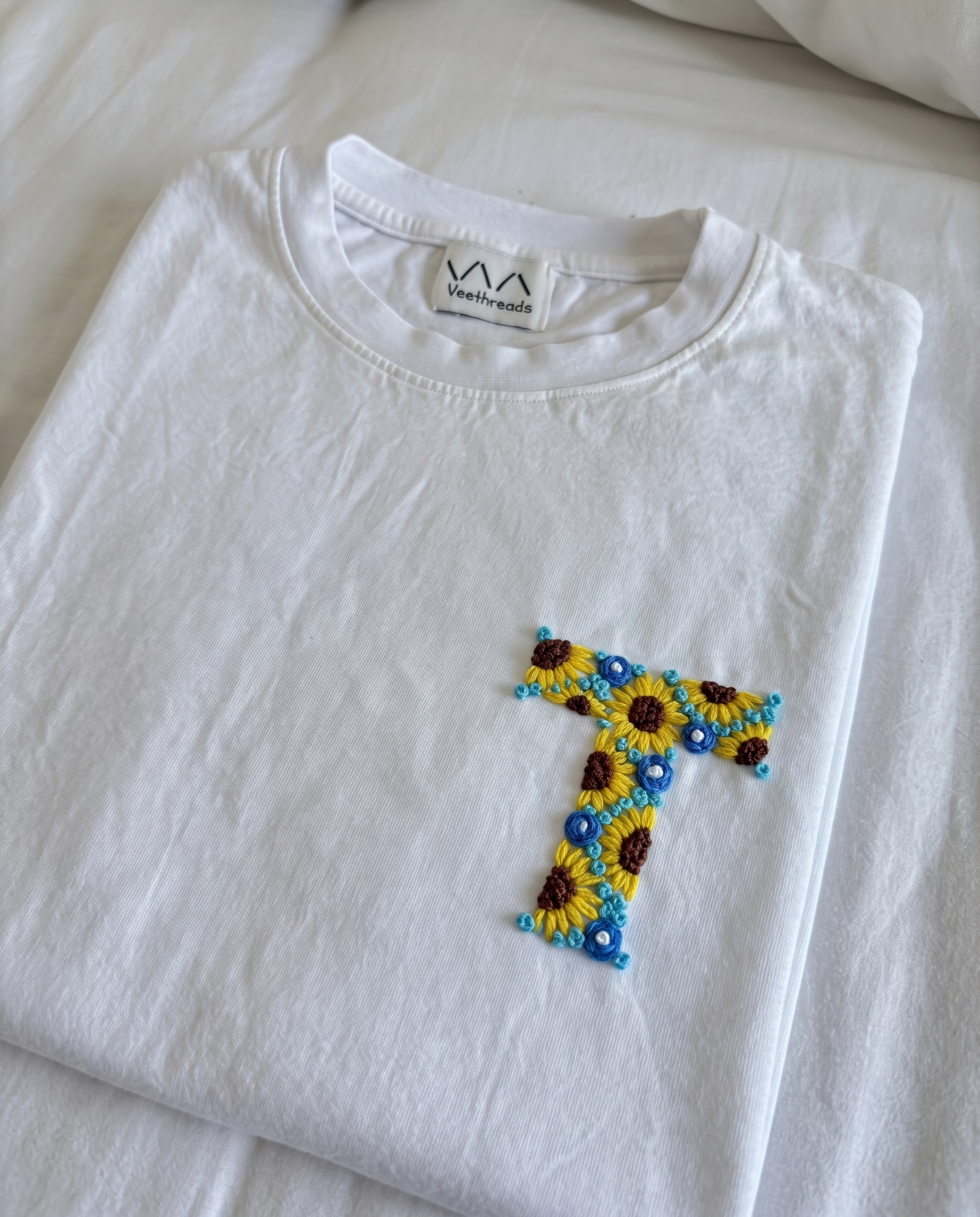Hand-embroidered floral initial, sunflowers and blue flowers, on a white cotton tee by Vee Threads