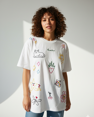 Woman wearing a white t-shirt with colorful doodles hand embroidered  on a plain background