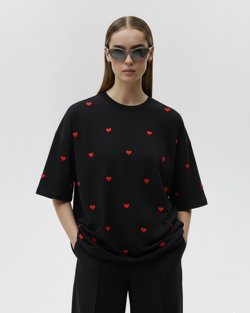 Person wearing a black t-shirt with red heart patterns on a plain background