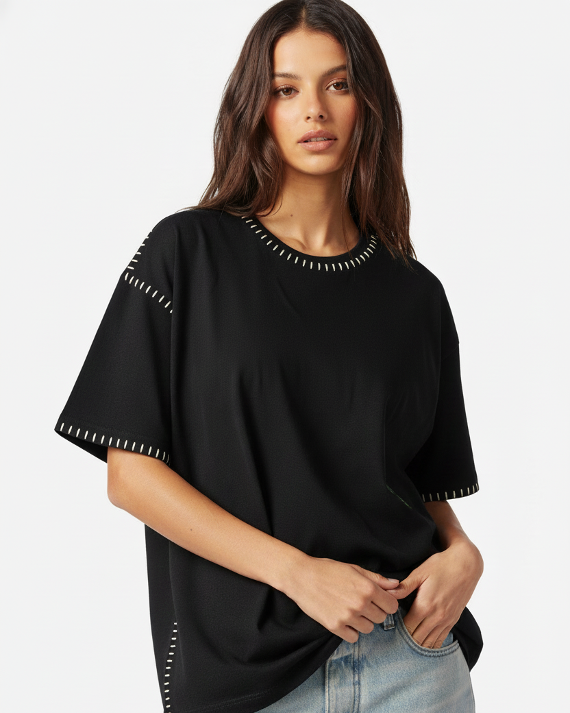 Woman wearing a black top with white trim embroidered  and light blue jeans on a white background