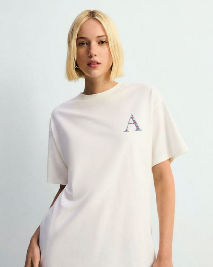 Person wearing a white shirt with a custom initial embroidered on a light gray background