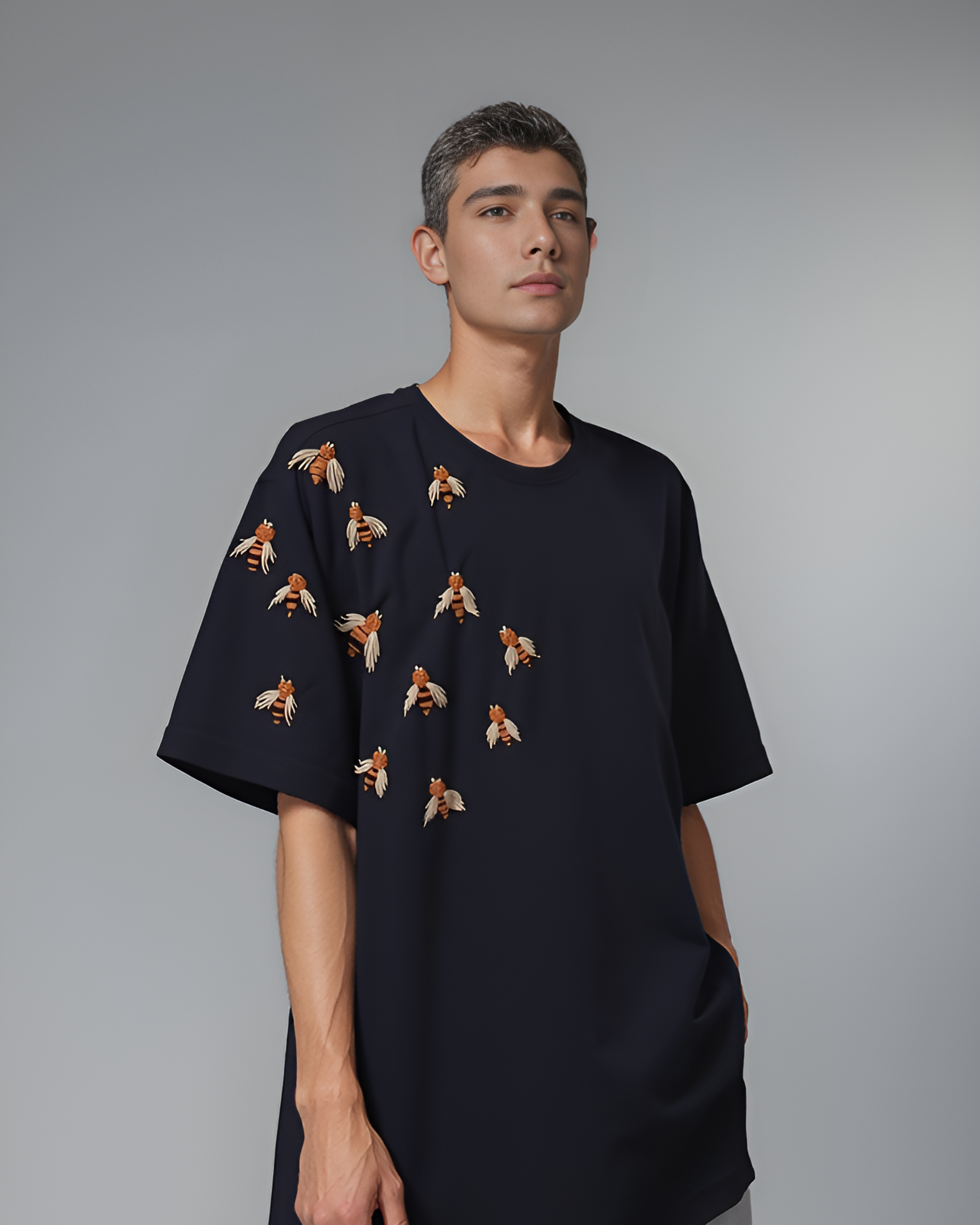 Model wearing oversized black t-shirt with hand-embroidered honey bee on the chest, styled with denim and sneakers.