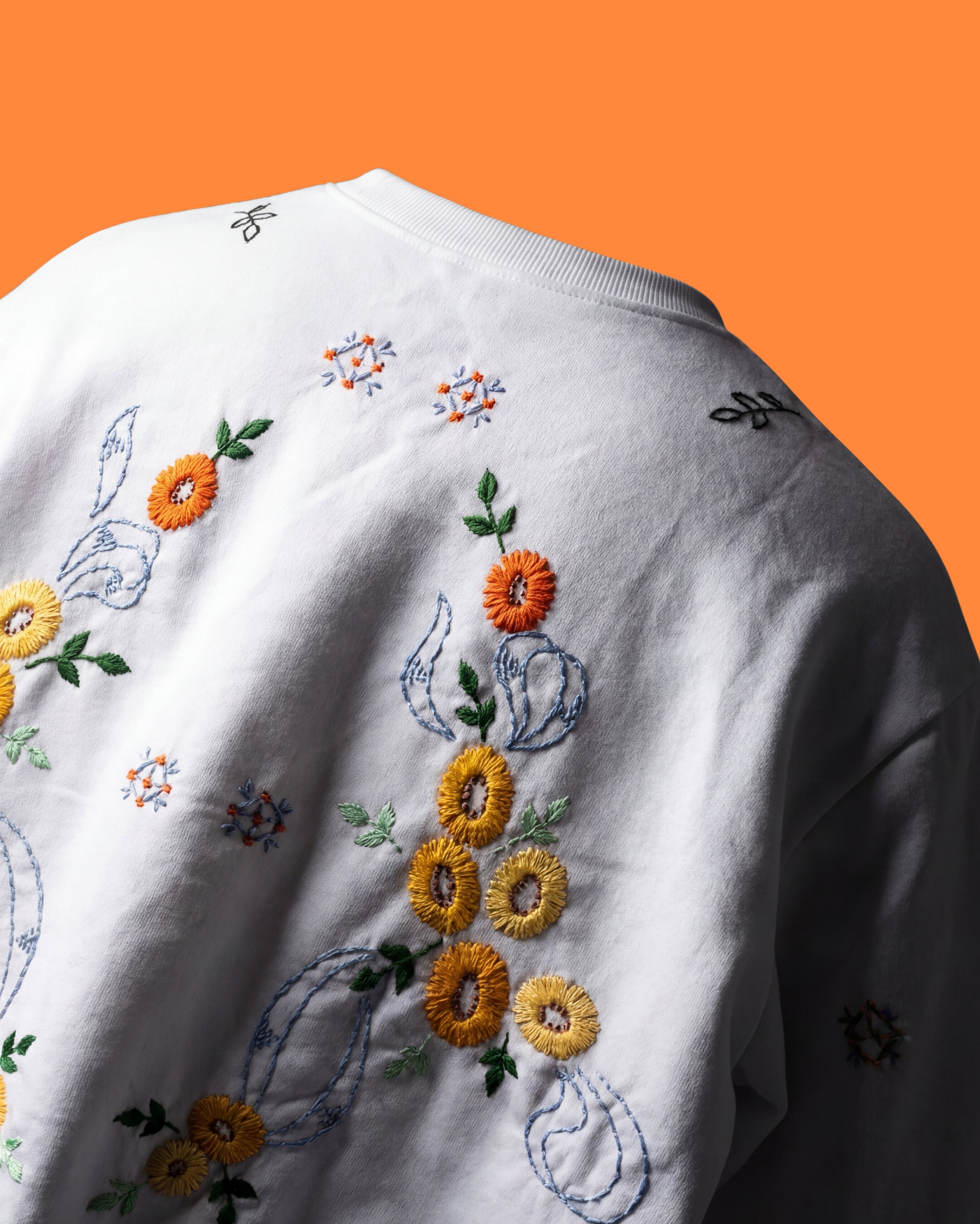 Embroidered floral design on a white garment against an orange background