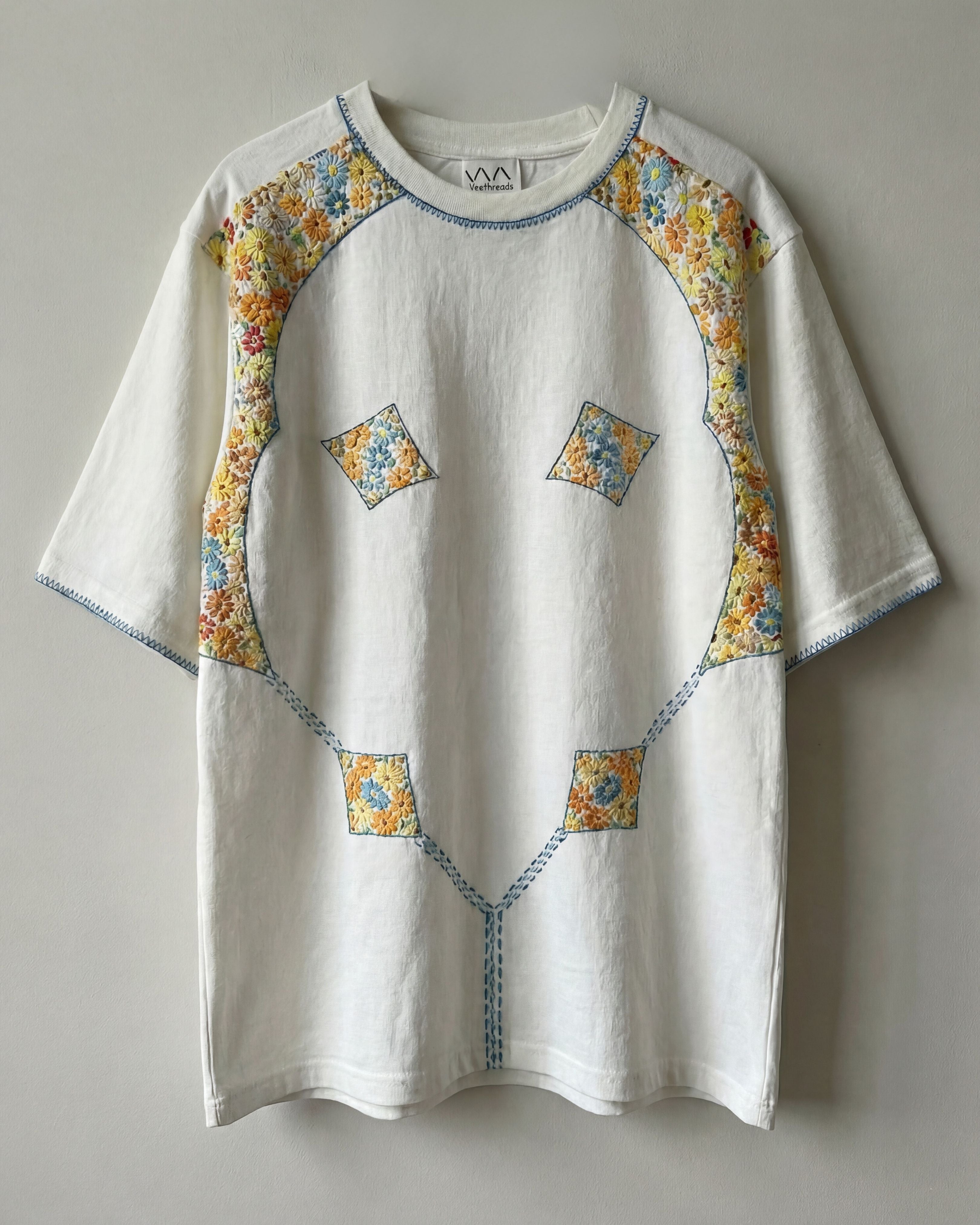 White shirt with floral embroidery patterns on sleeves and chest against a gray background