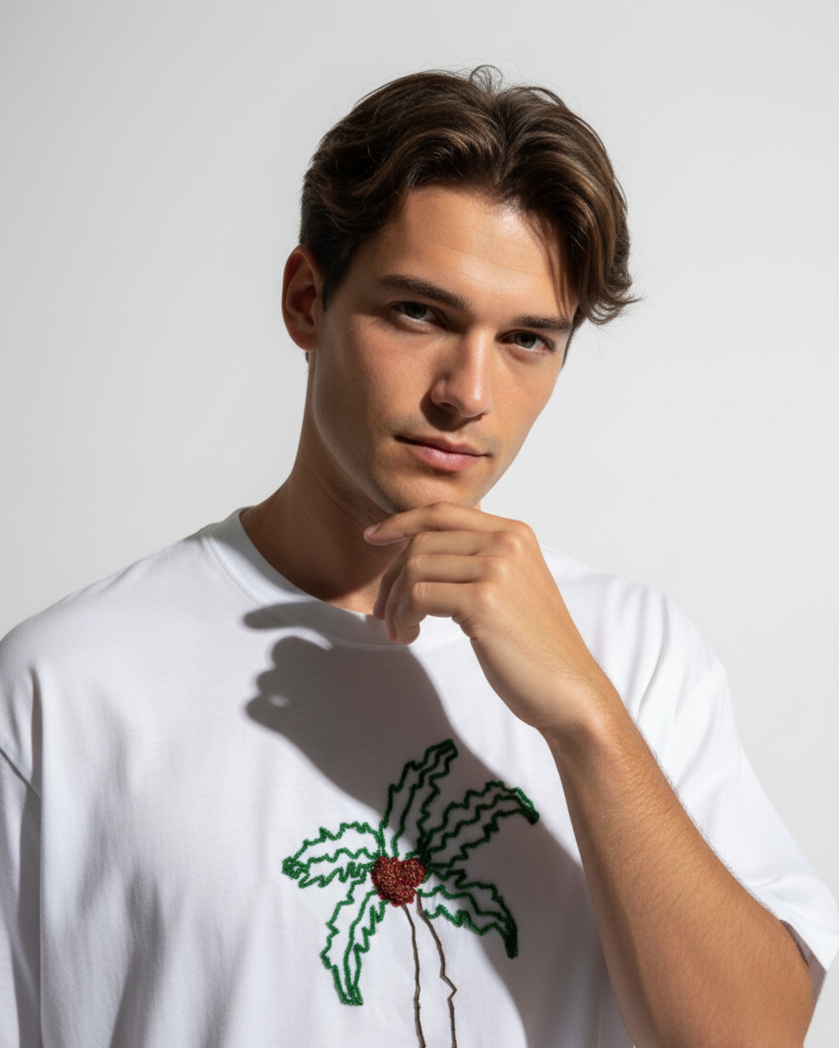Man wearing a white t-shirt with a bead embroidered on a plain background
