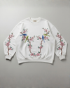White sweatshirt with floral and bird designs han dembroidery  on a gray background
