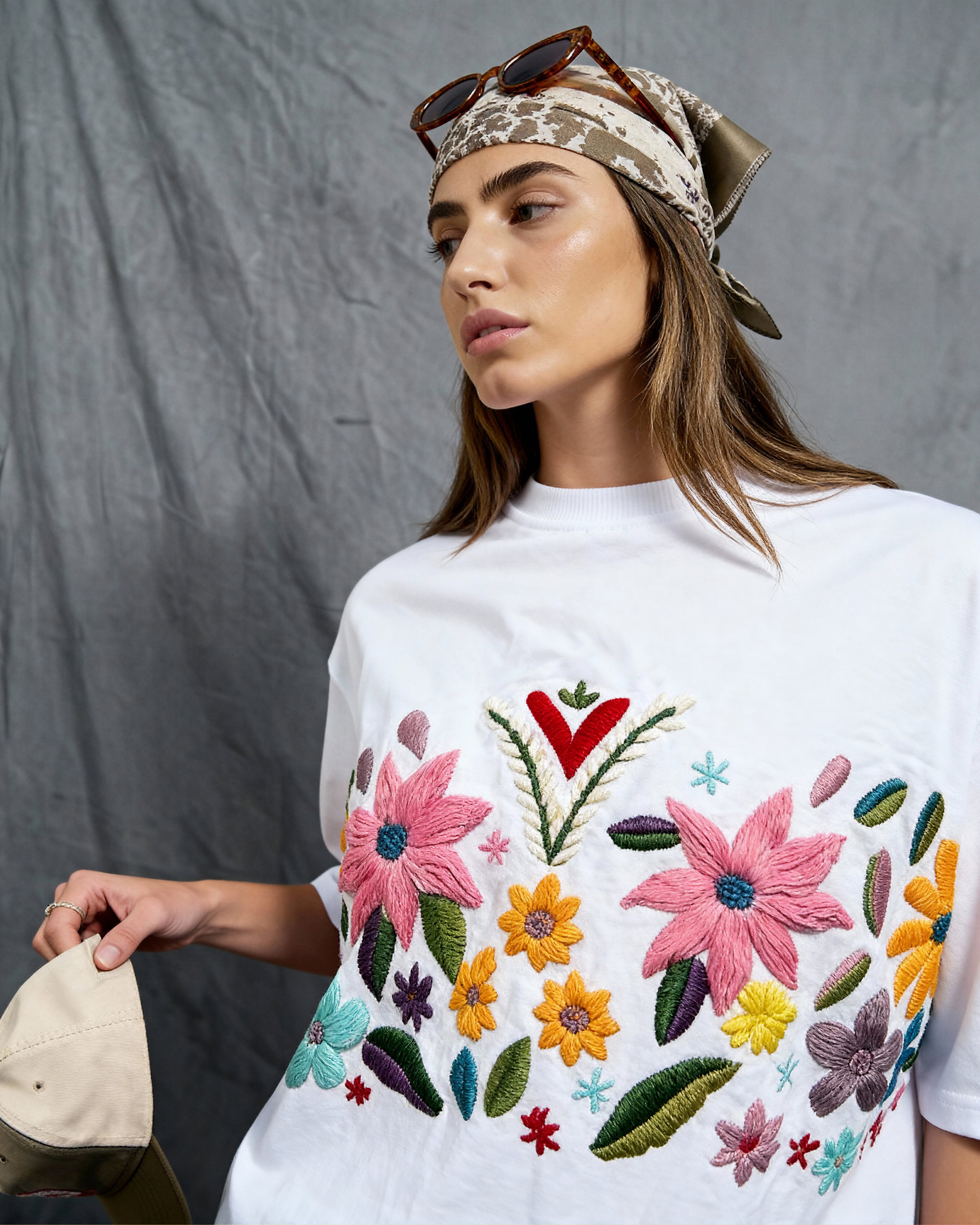 Woman wearing a white t-shirt with colorful floral embroidery against a gray background