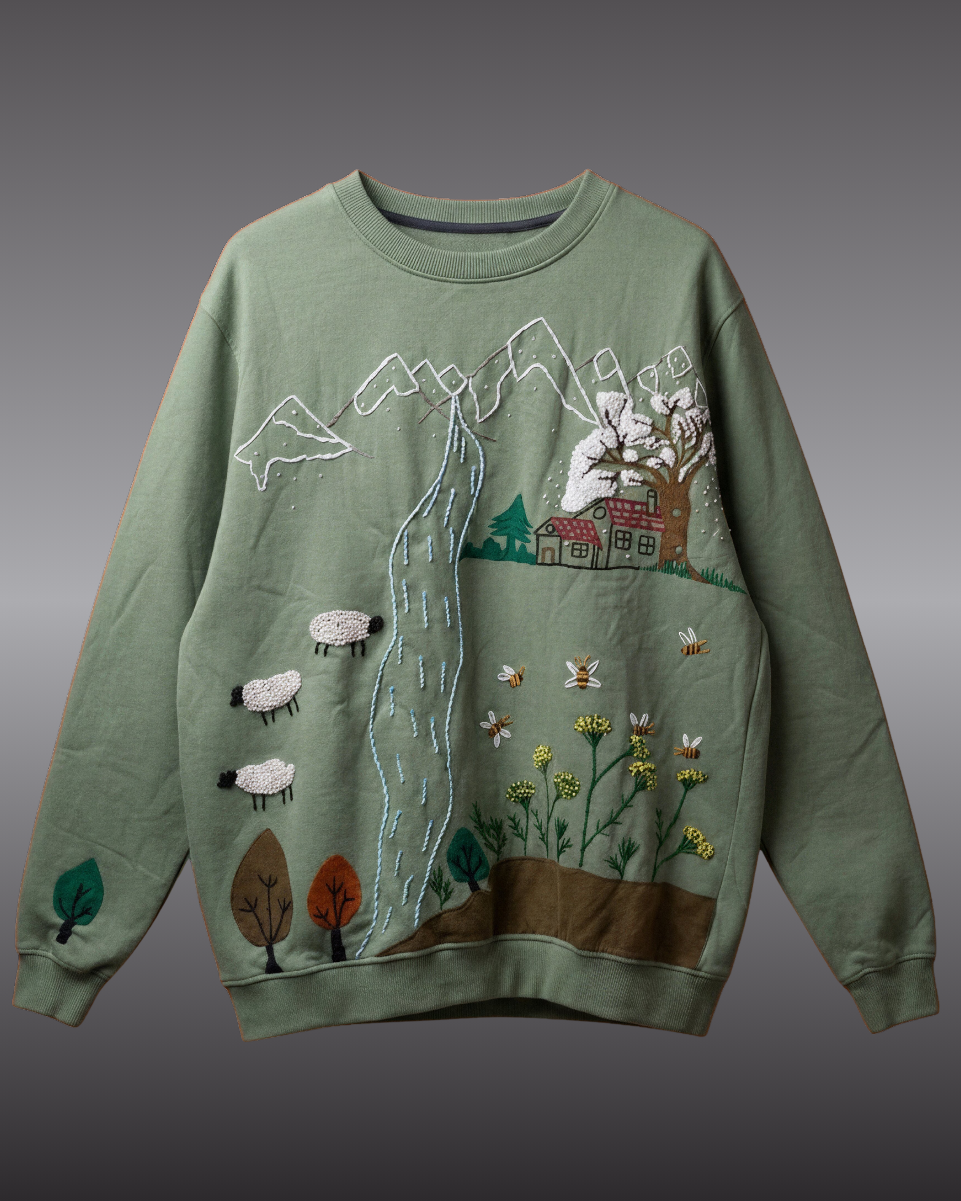 Green sweater with hand embroidered landscape design on a gray background