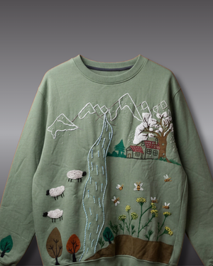 Green sweater with embroidered landscape design on a gray background