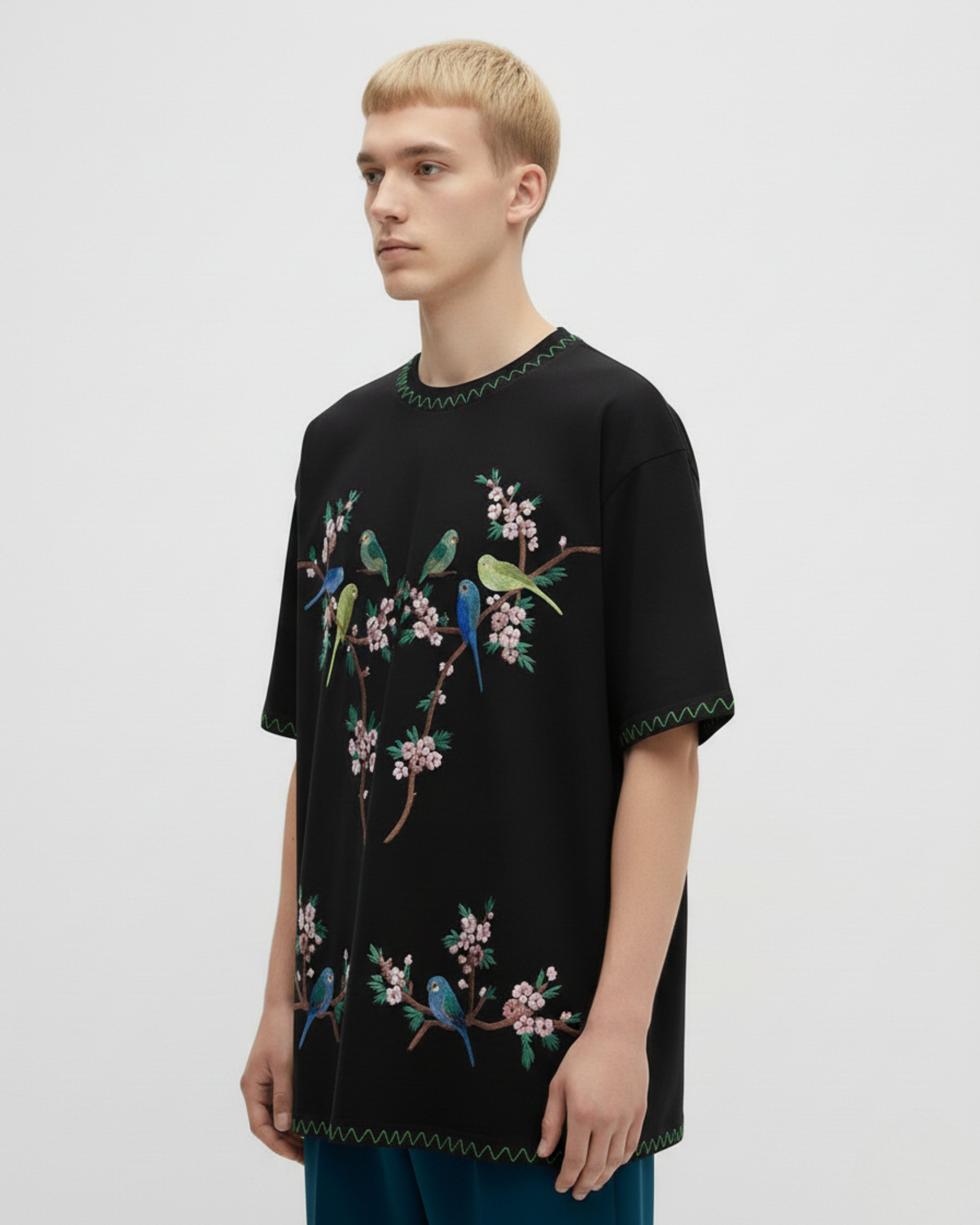 Person wearing a black t-shirt with colorful bird and floral embroidery on a light gray background