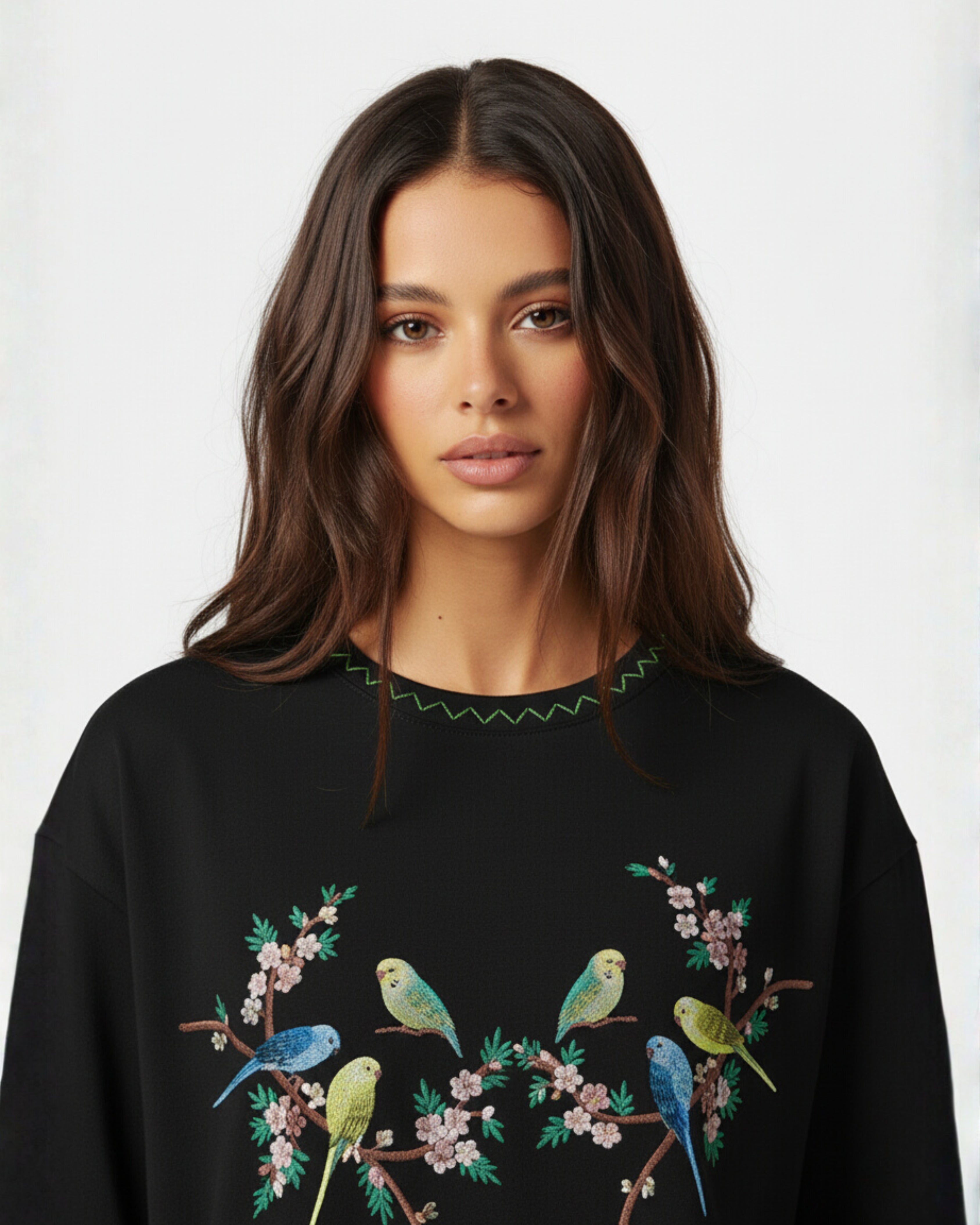 Woman wearing a black sweater with colorful bird and floral embroidery on a white background