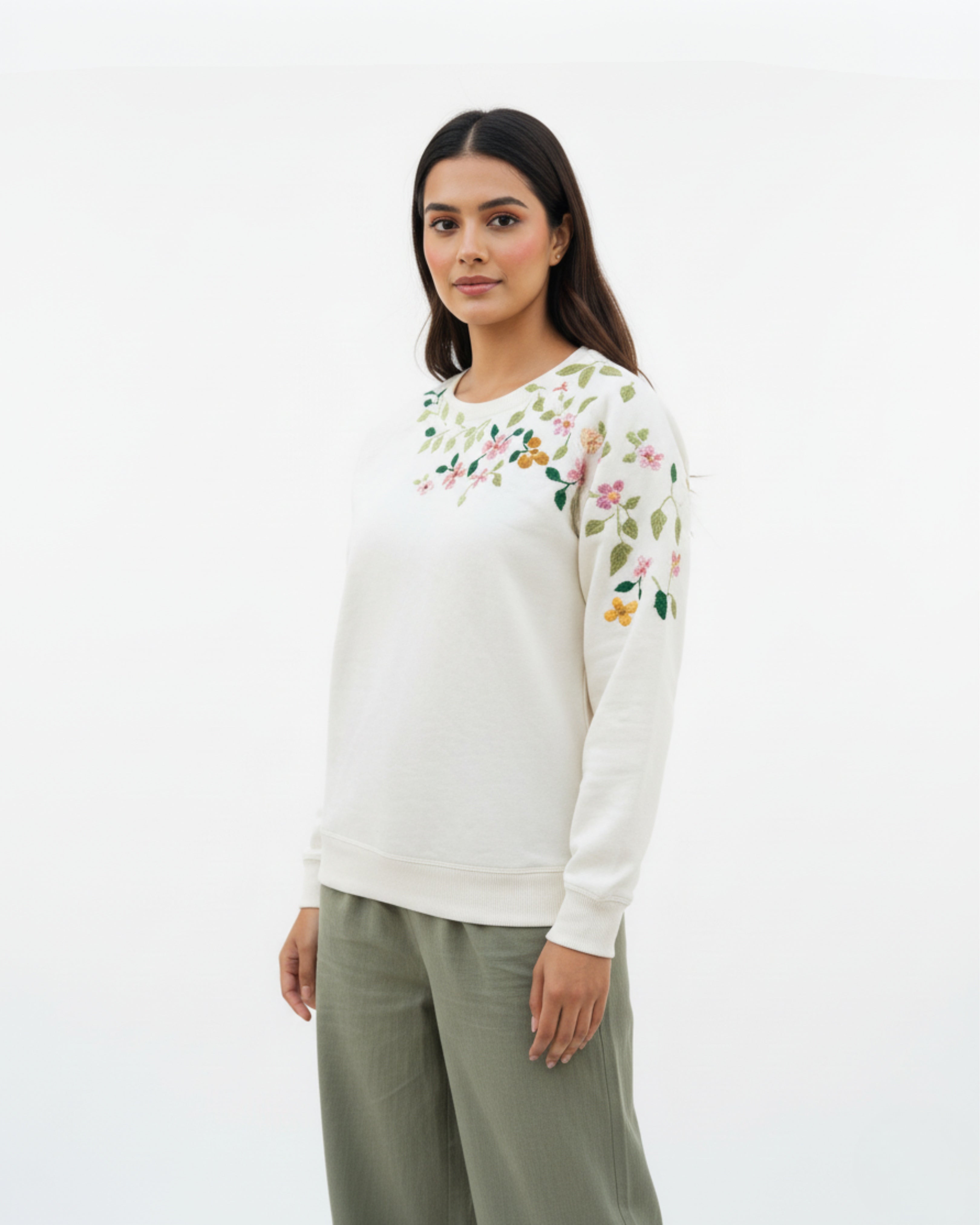 Woman wearing a white sweater with floral patterns on a plain background