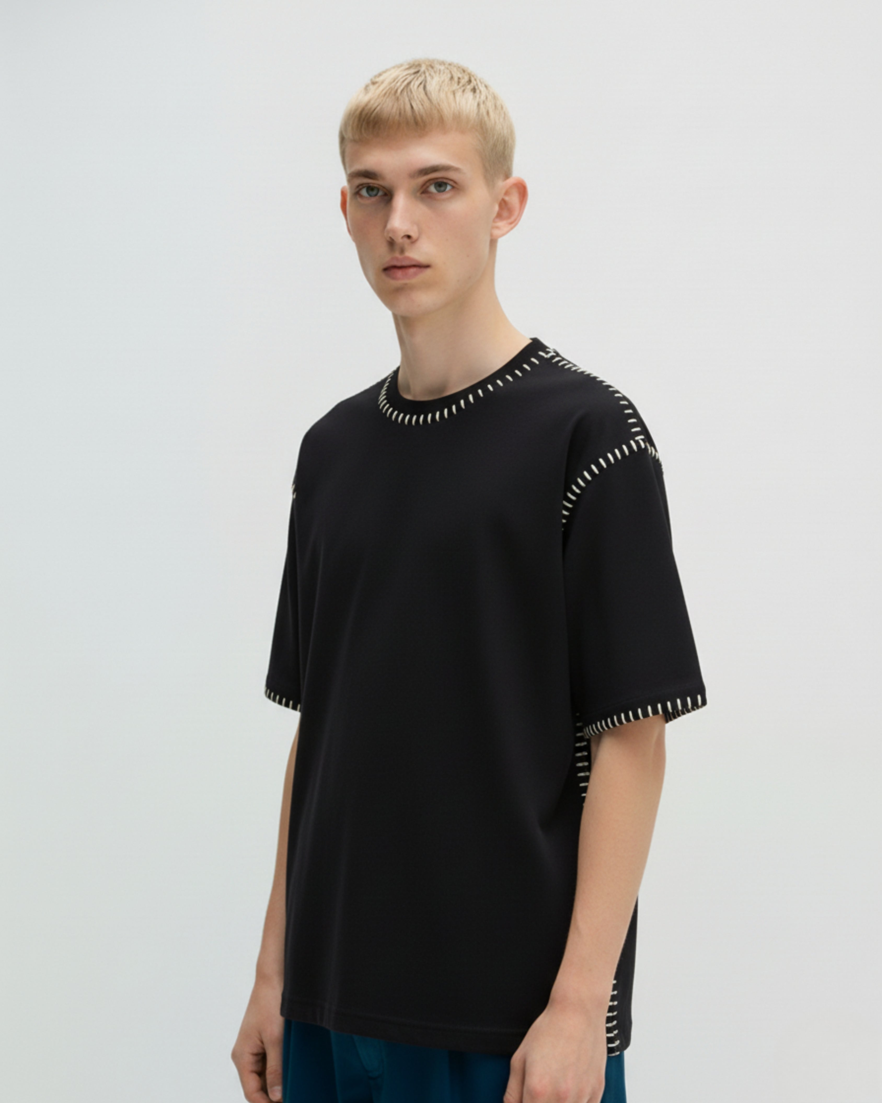 Person wearing a black t-shirt with embroidered decorative elements on a plain background