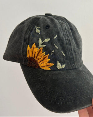 Black baseball cap with sunflower embroidery on a light gray background