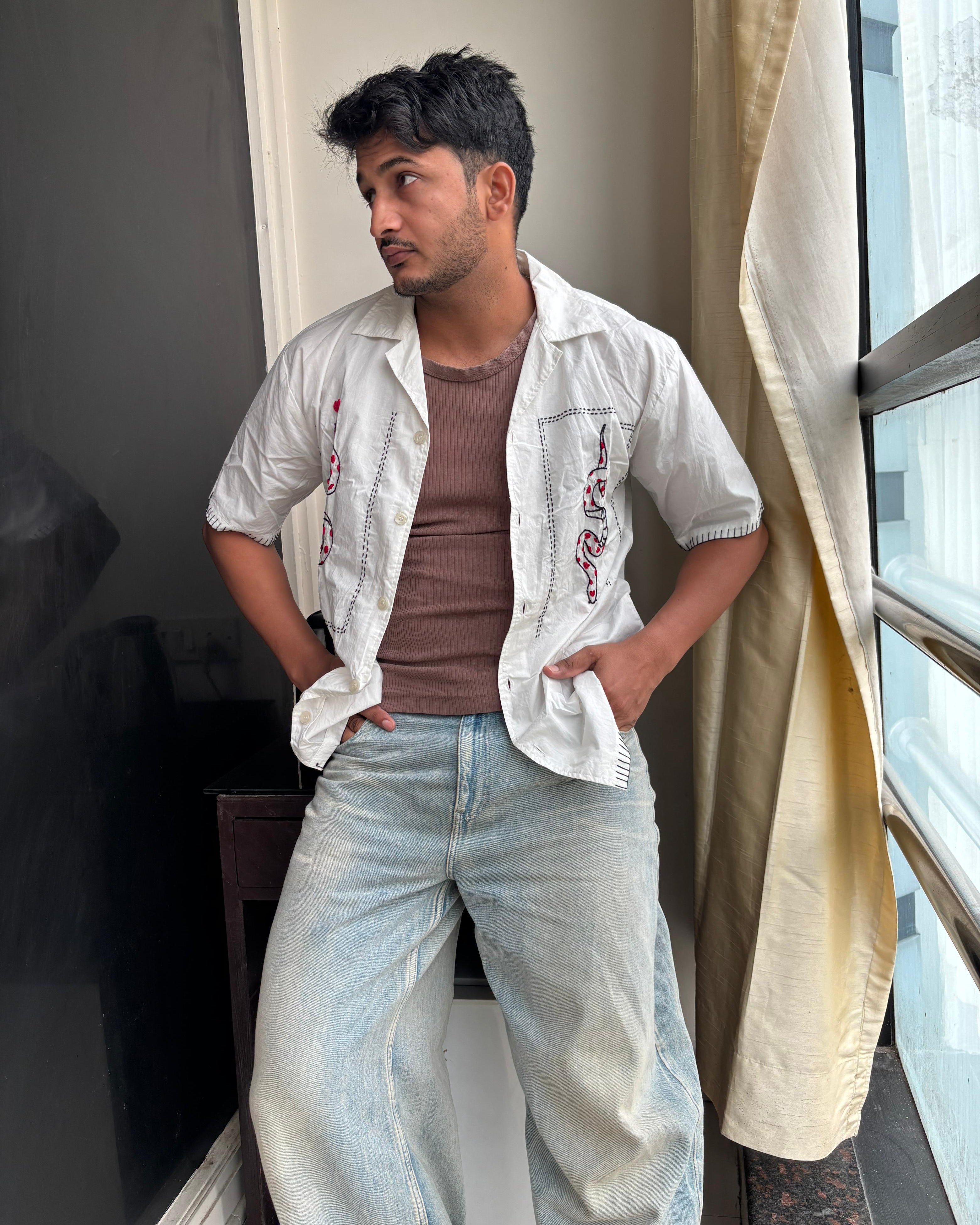 Close-up of a cream cotton shirt with hand-embroidered red heart and black snake motifs, showcasing detailed Indian-inspired craftsmanship and bold contrast stitching.