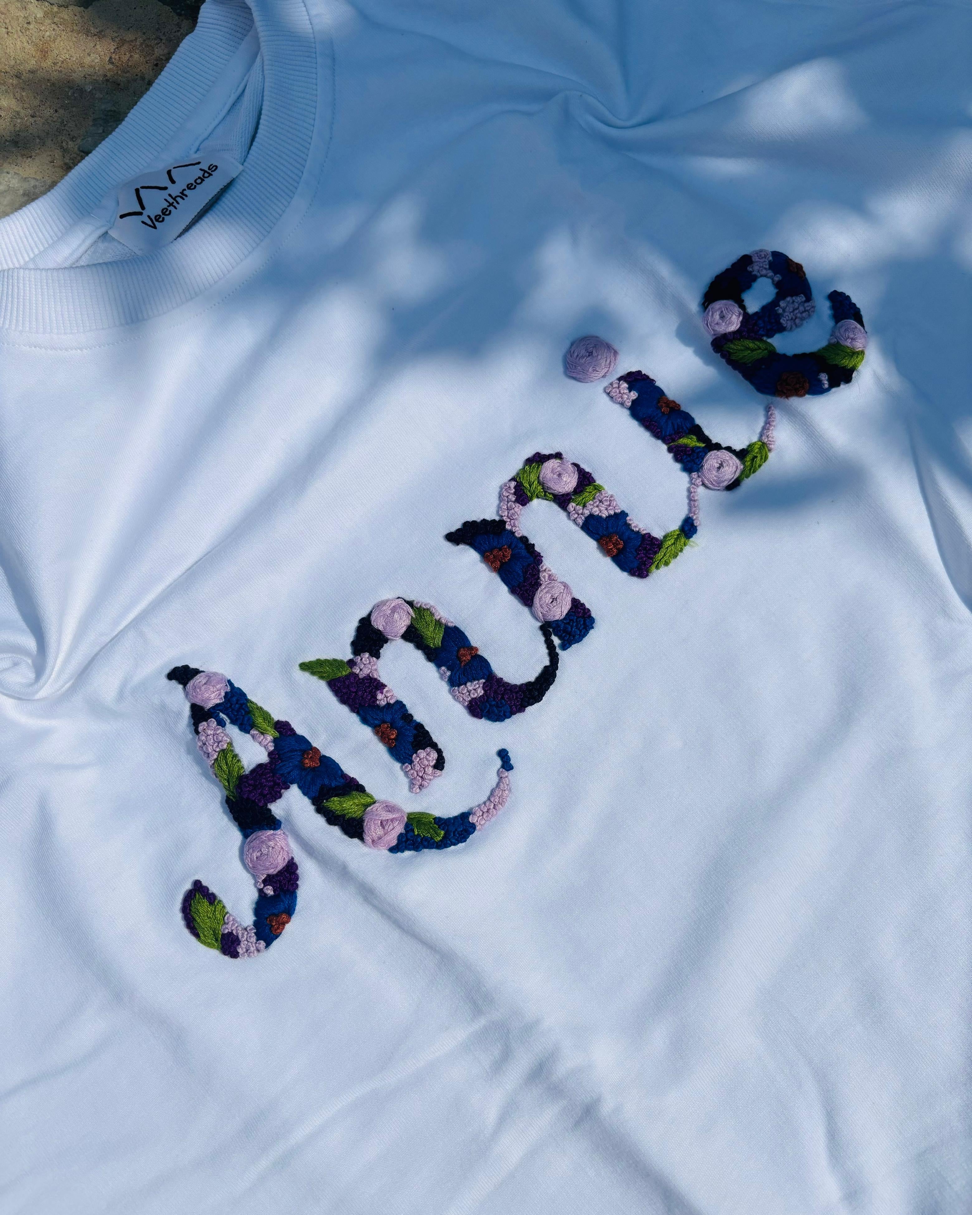 White t-shirt with floral embroidered text on a white background