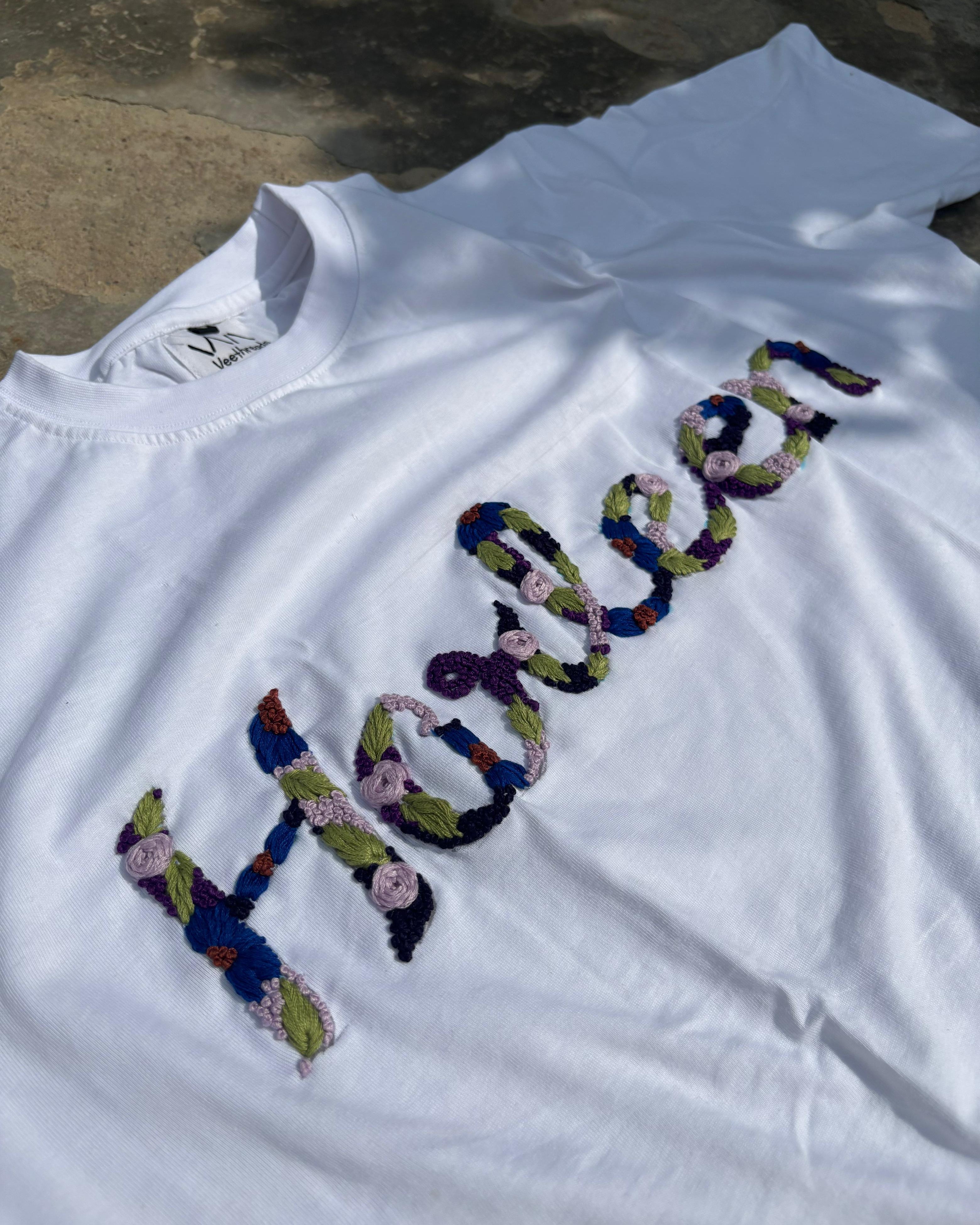 White t-shirt with colorful custom embroidered text on a textured surface