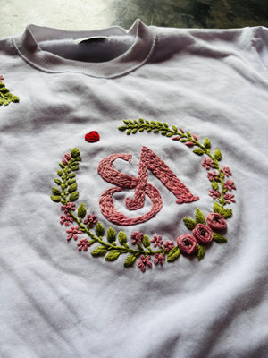 Embroidered design on a white sweatshirt with pink letter 'S' and floral elements.