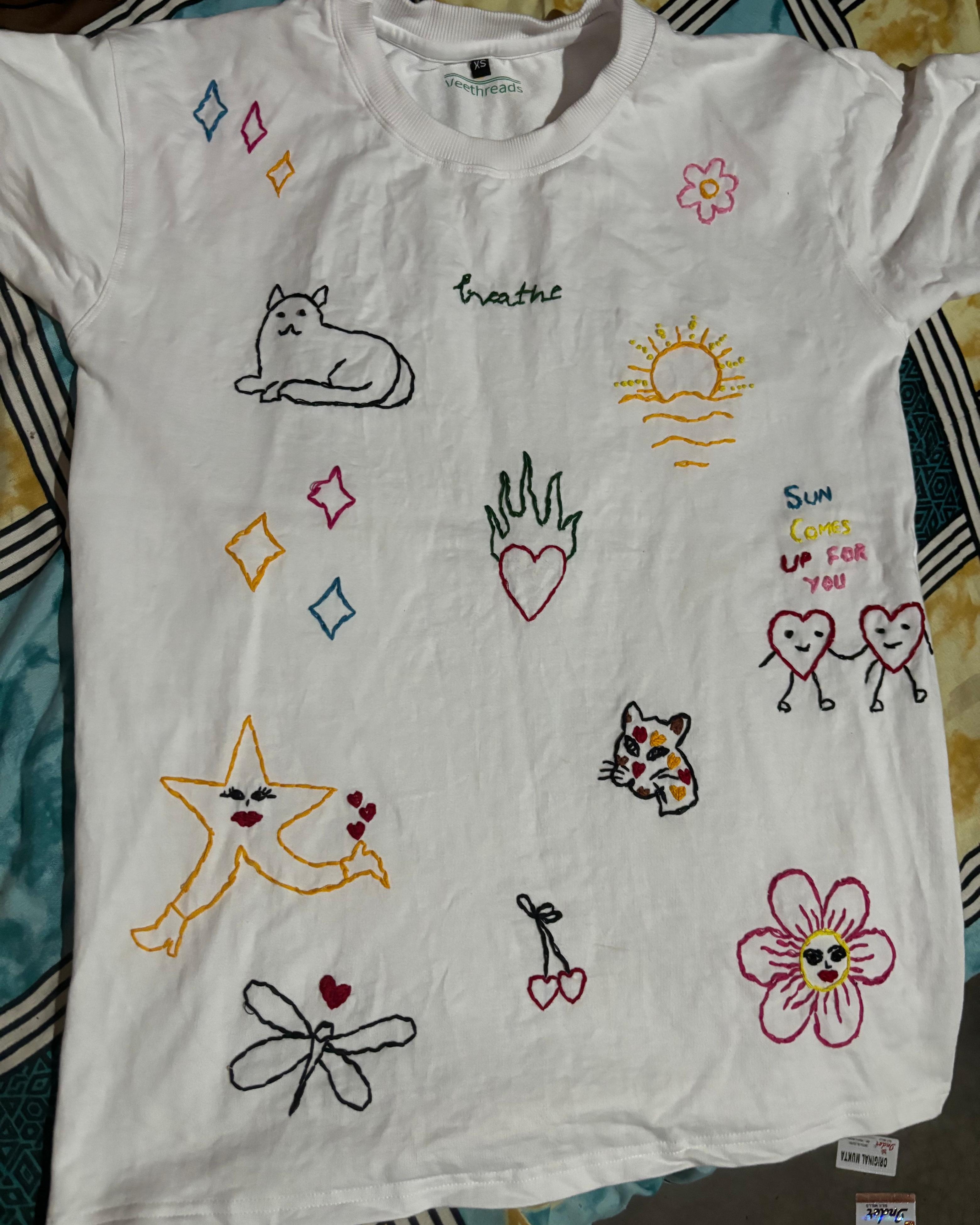 White t-shirt with colorful embroidered designs on a patterned fabric background