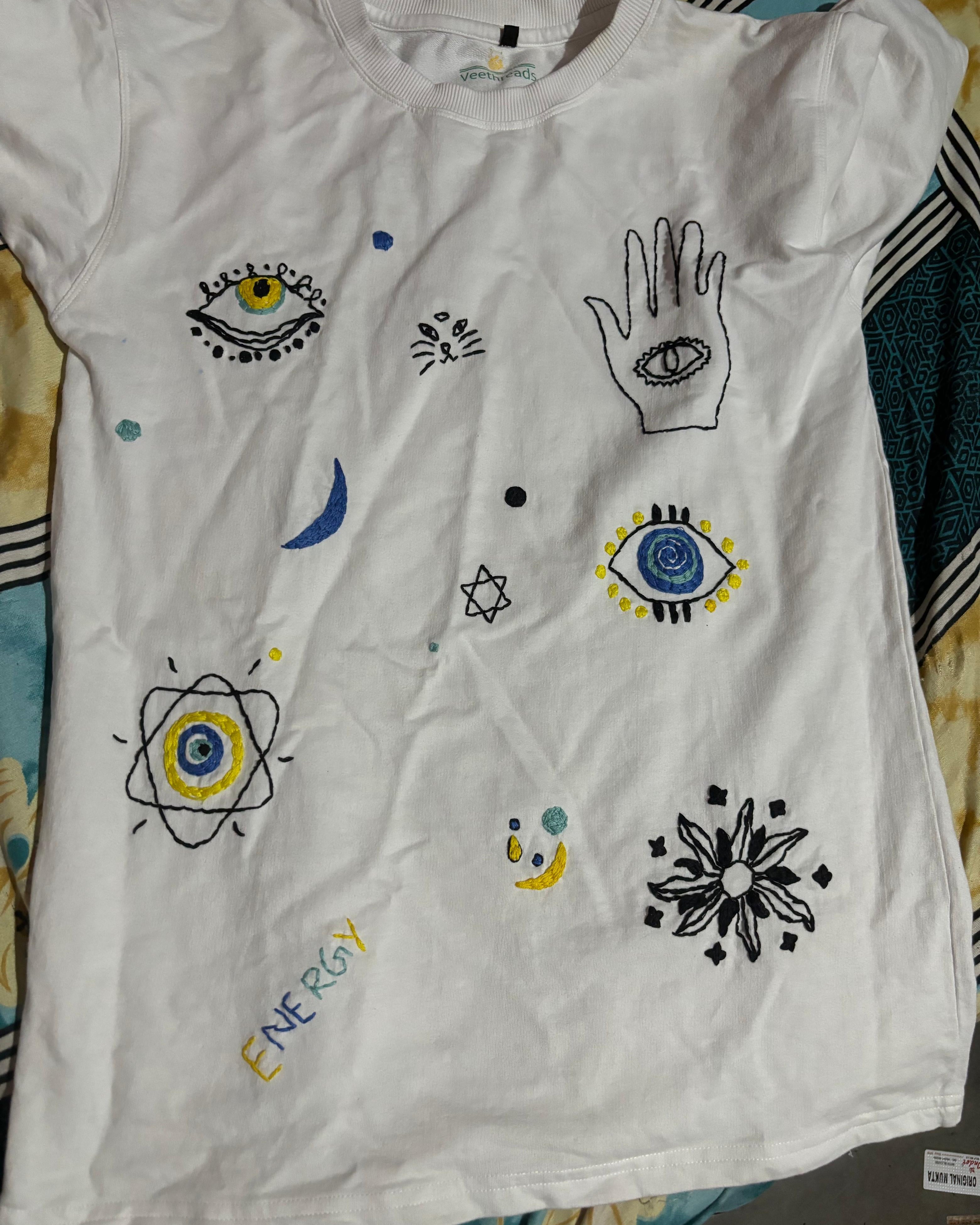 White t-shirt with various symbols and designs on a patterned fabric background
