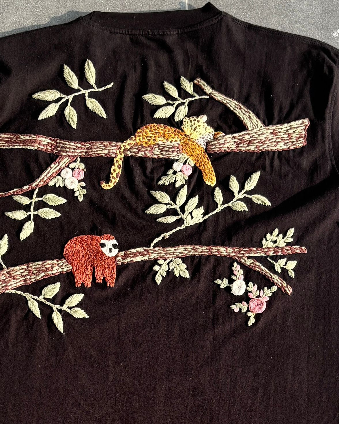 Black t-shirt with embroidered sloths and branches on a gray background