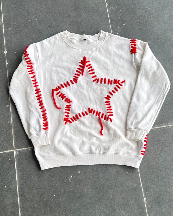 White sweatshirt with red star design on a gray tiled floor