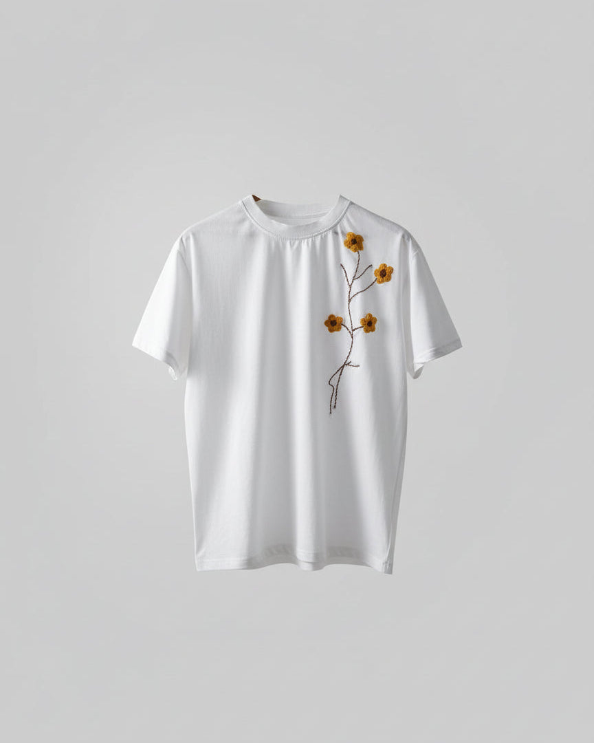 White garment with embroidered brown flowers and leaves on a blurred natural background