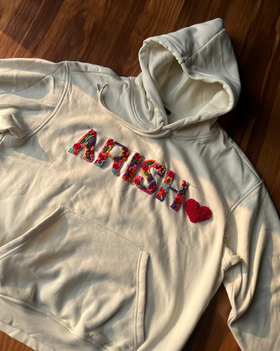 Beige hoodie with colorful text on a wooden surface