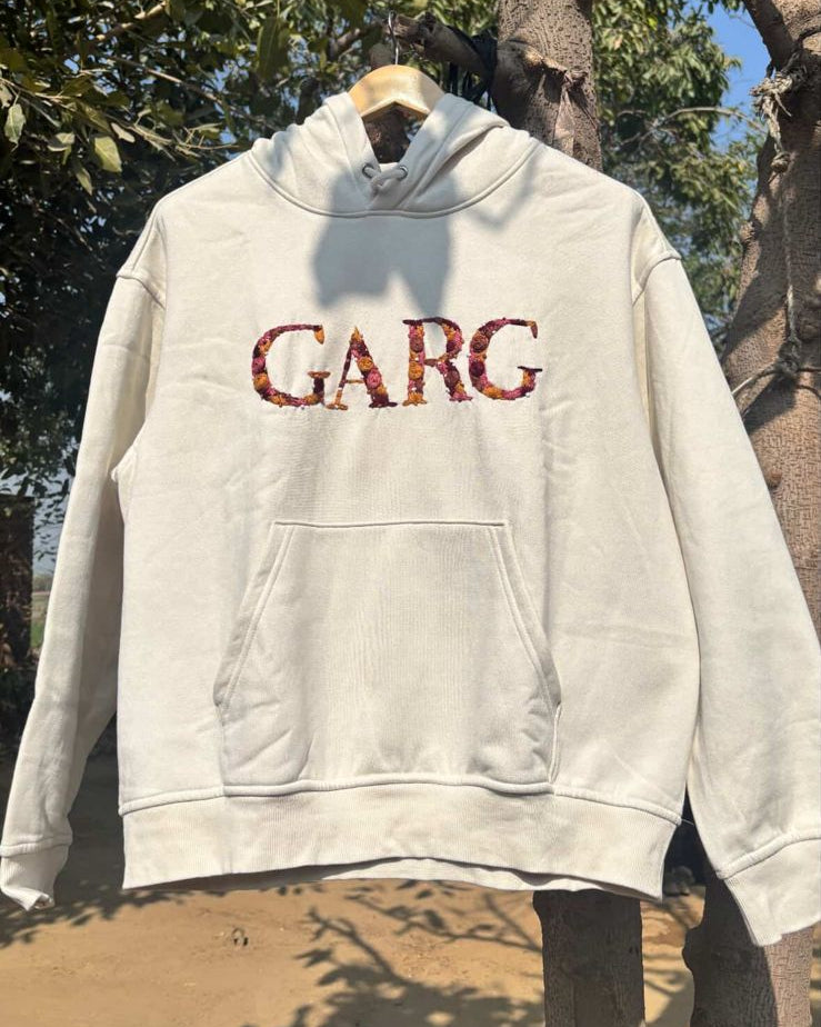 White hoodie with red text 'GARC' custom name embroidered hanging outdoors against a natural background