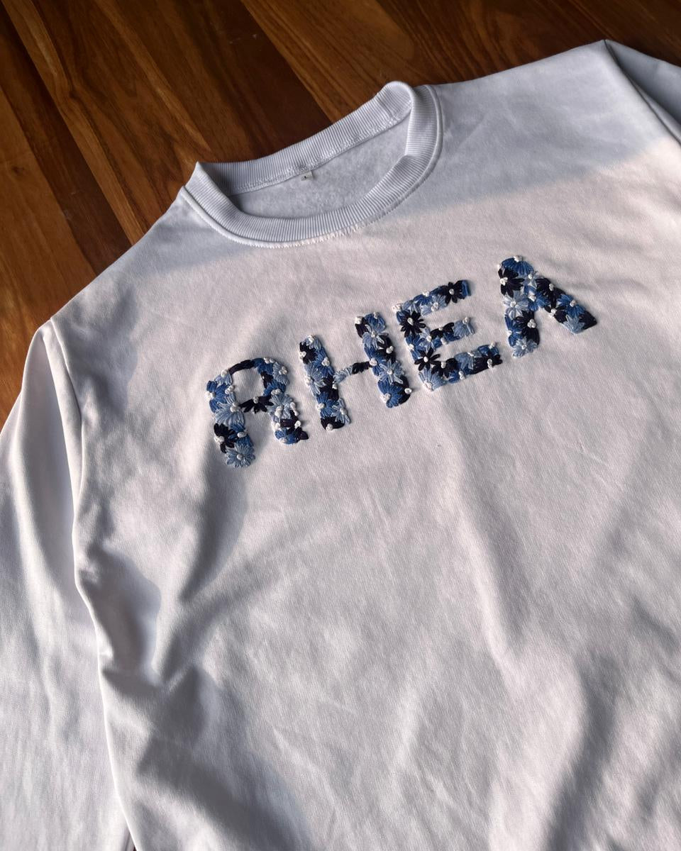 White customised name sweatshirt with 'AHEA' printed on it, laid flat on a wooden surface.