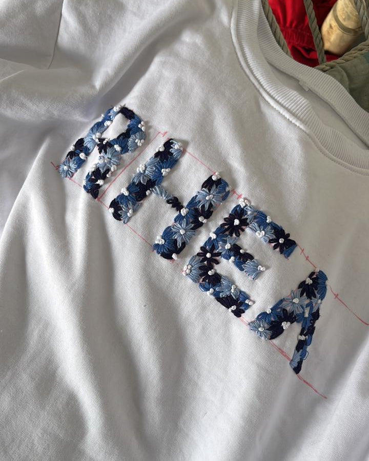 White sweatshirt with blue floral text on a wooden surface