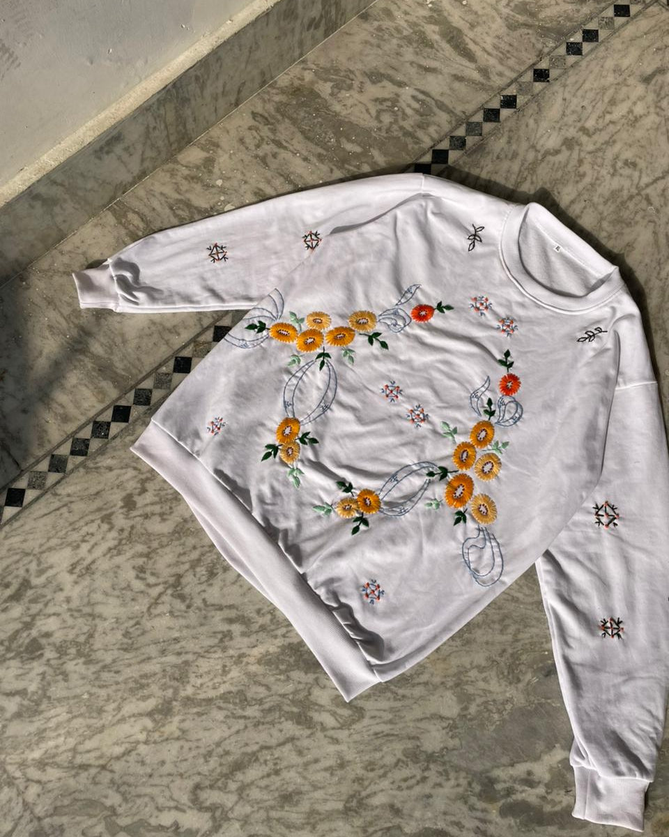 White long-sleeve shirt with floral embroidery on a stone floor
