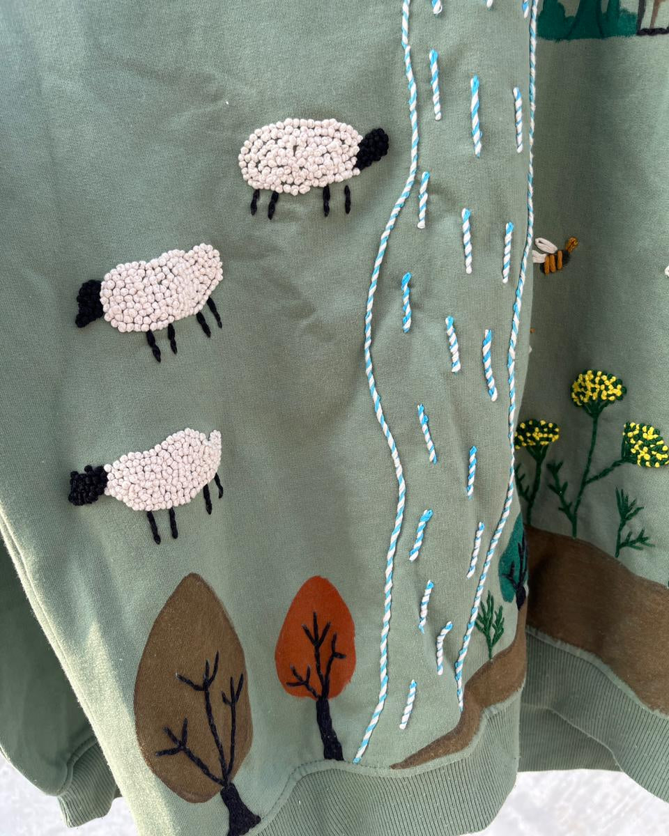 Textile with embroidered sheep and nature scenes on a green background