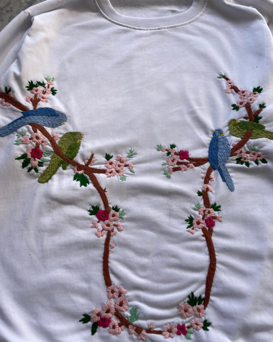 White sweatshirt with embroidered birds and flowers on a branch design.
