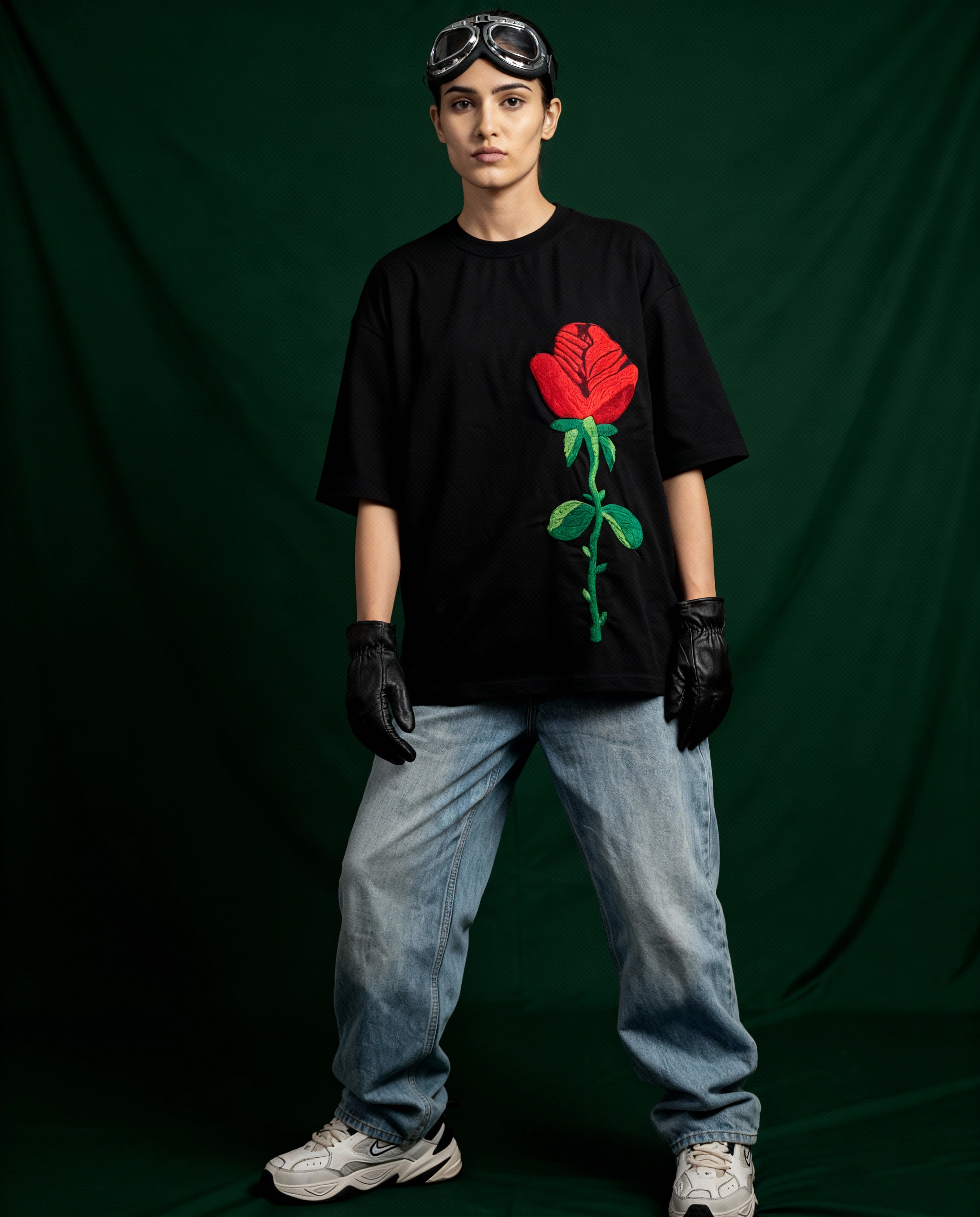 Person wearing a black t-shirt with a red rose graphic, blue jeans, and black gloves on a dark green background.