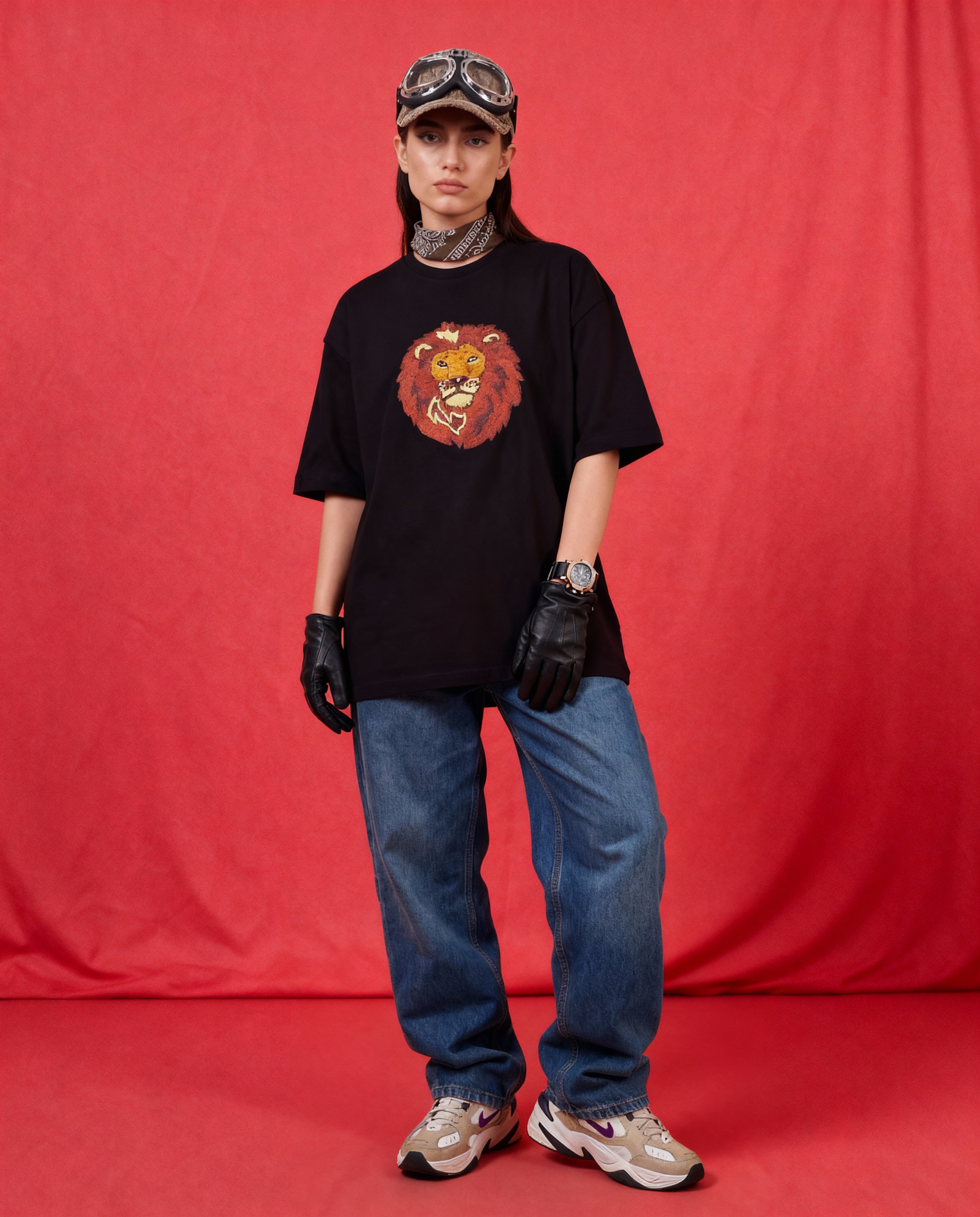 Person wearing a black t-shirt with a lion graphic, blue jeans, and a cap against a red background