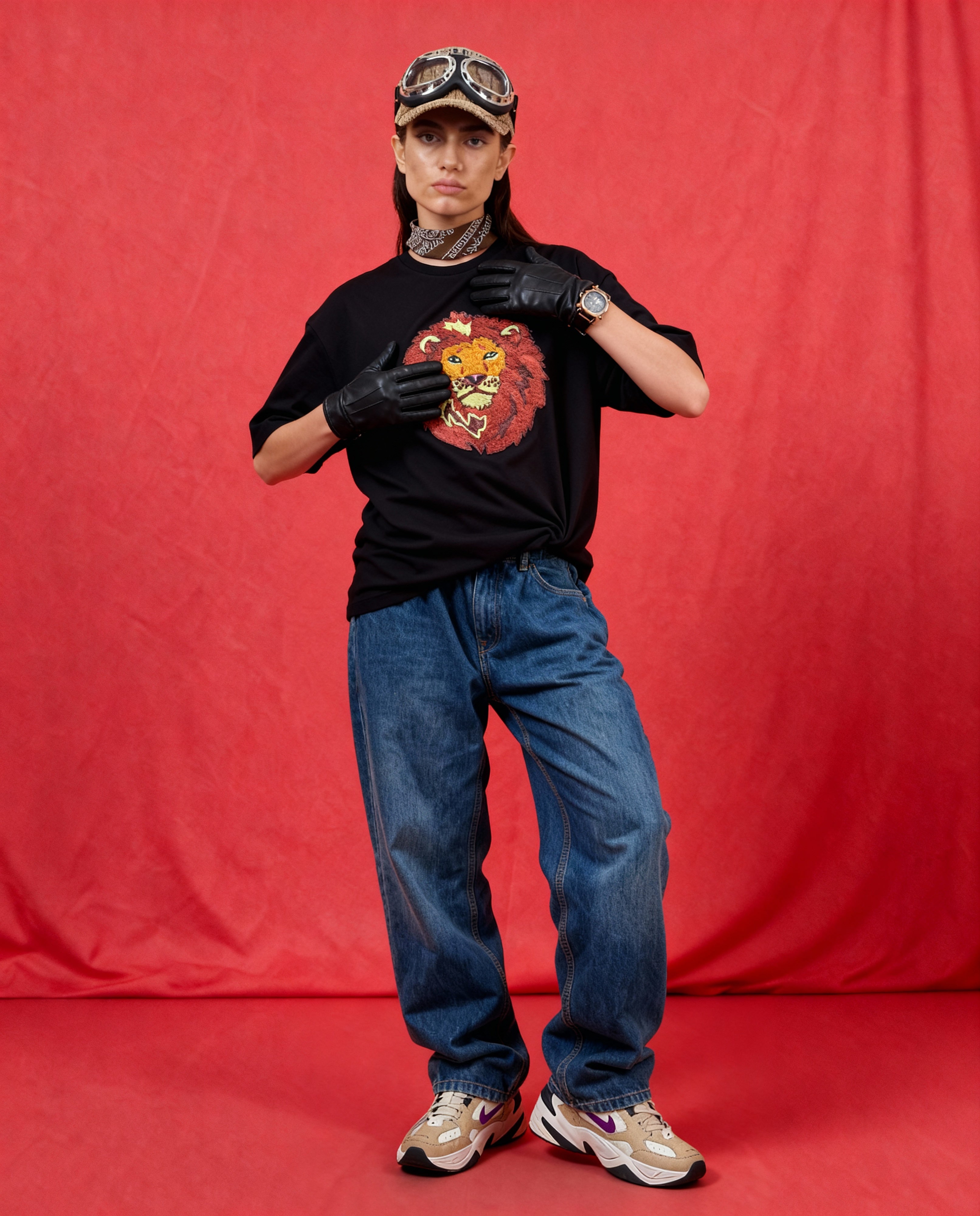 Person wearing a black t-shirt with a lion graphic, blue jeans, and a cap against a red background