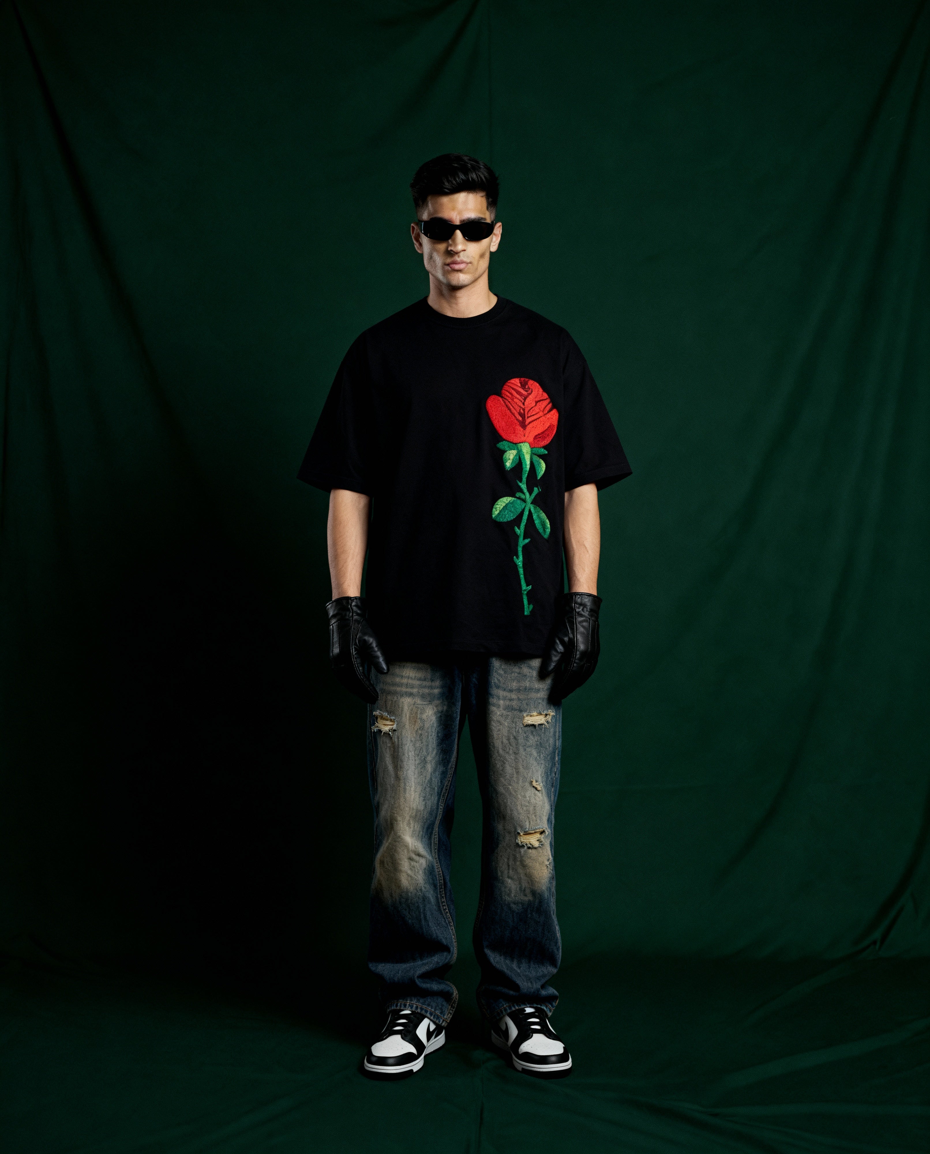 Person wearing a black t-shirt with a red rose design embroidered , standing against a dark green backdrop.