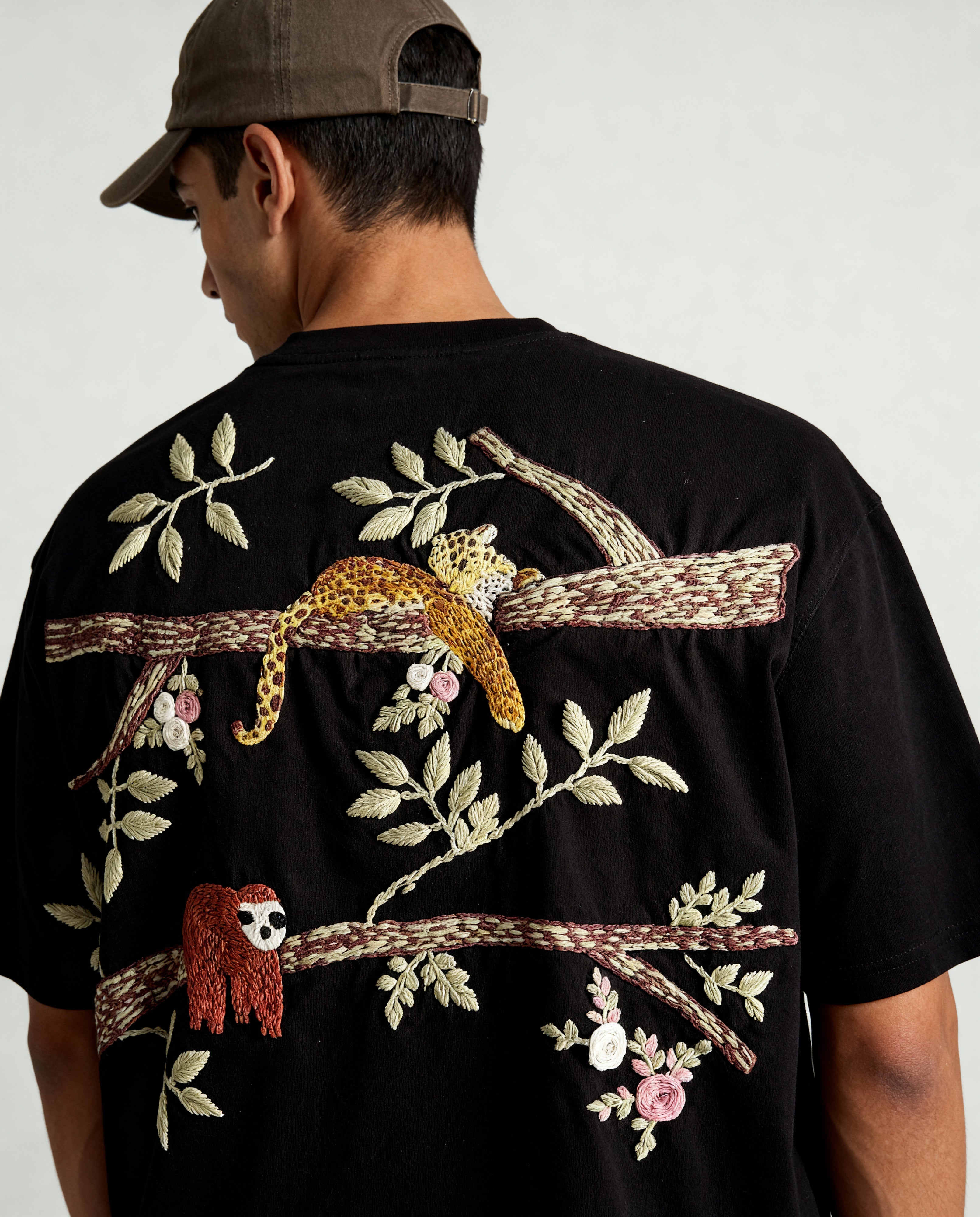 Person wearing a black t-shirt with colorful embroidered designs on the back.