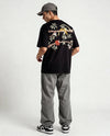 Person wearing a black t-shirt with floral designs hand embroidered on the back, standing against a white background
