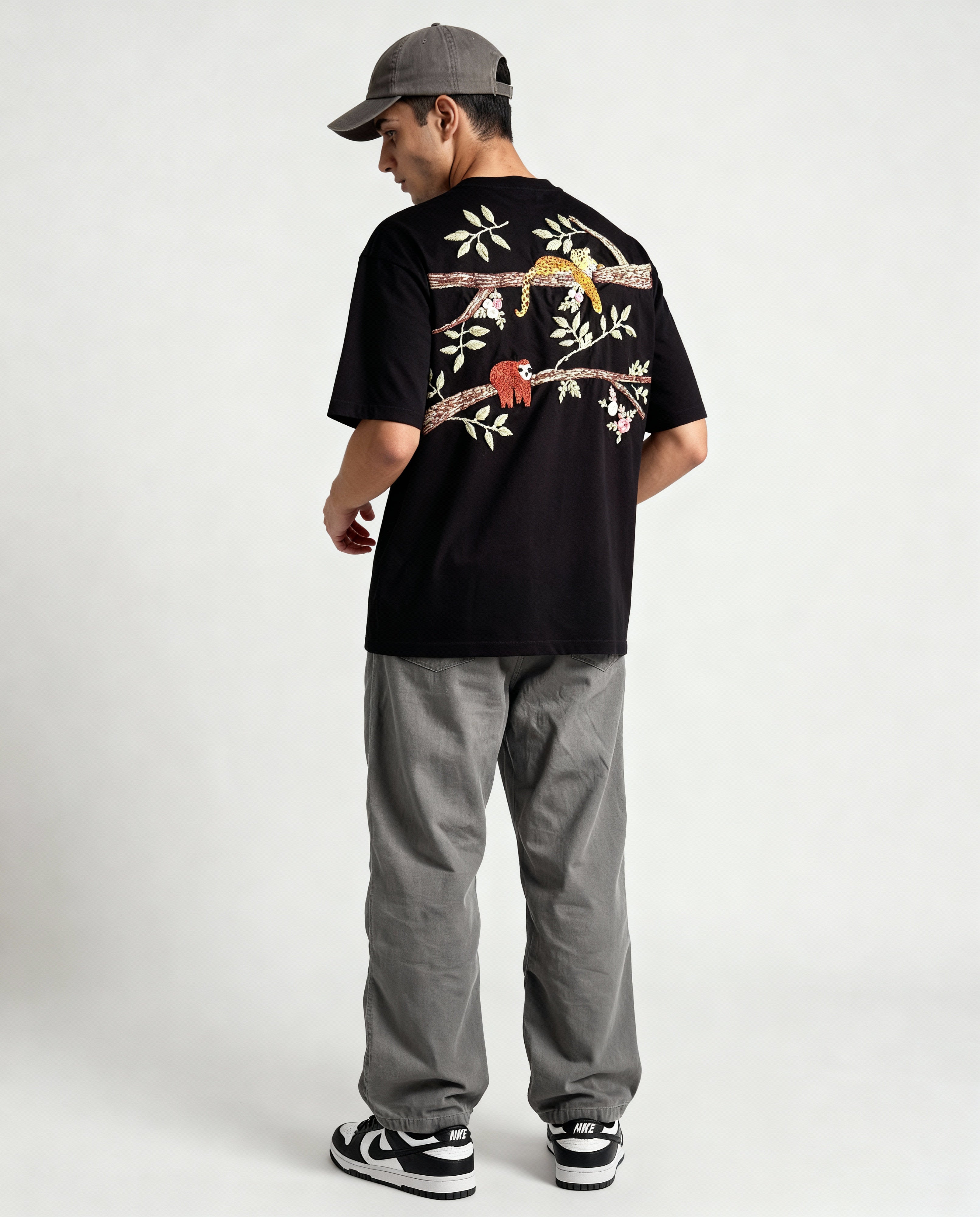 Person wearing a black t-shirt with floral designs hand embroidered on the back, standing against a white background