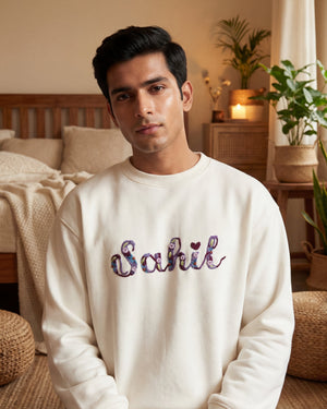 Man wearing a white sweatshirt with 'Sahil' custom name embroidered  on it in a bedroom setting.