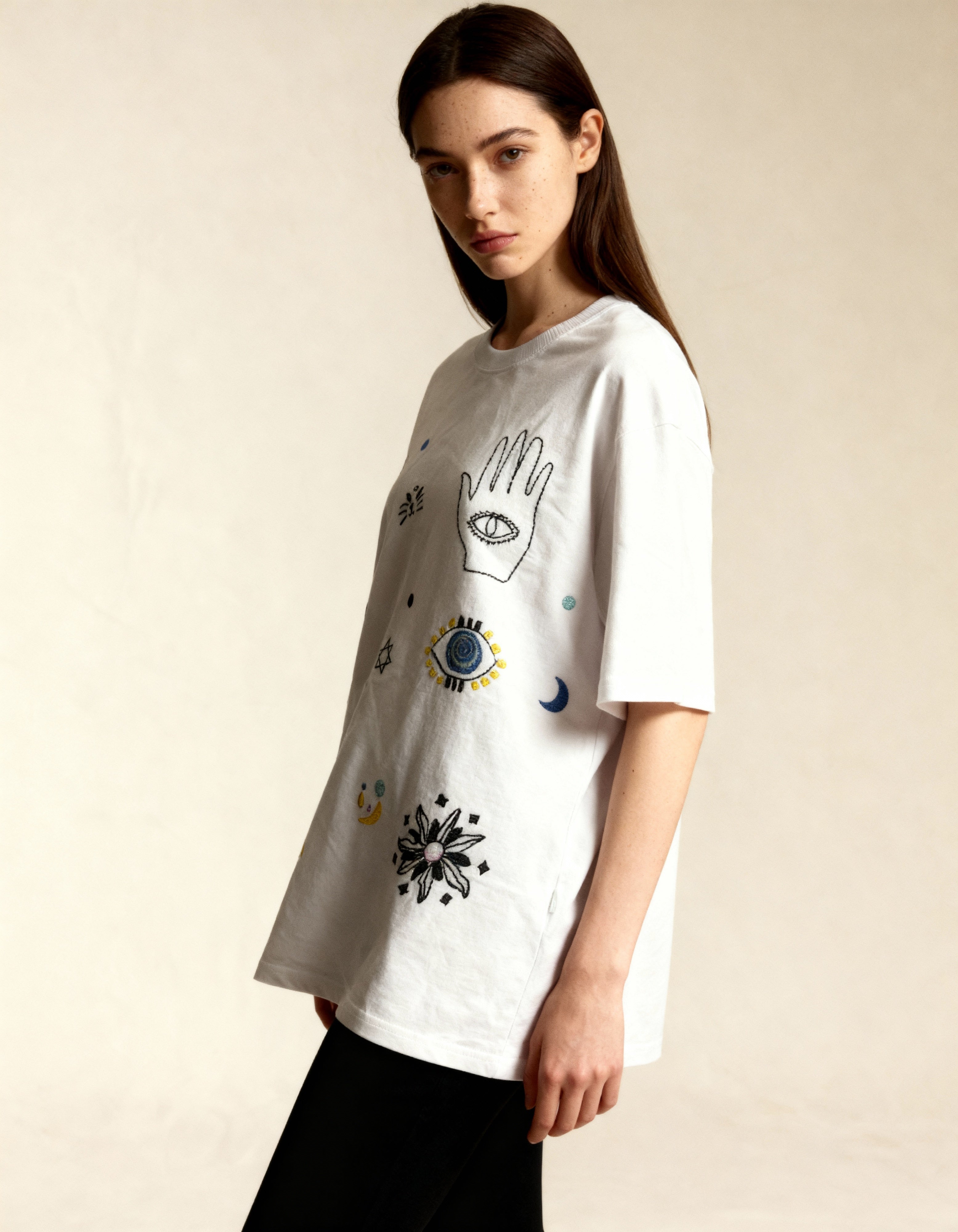 Person wearing a white t-shirt with embroidered graphic designs on a beige background