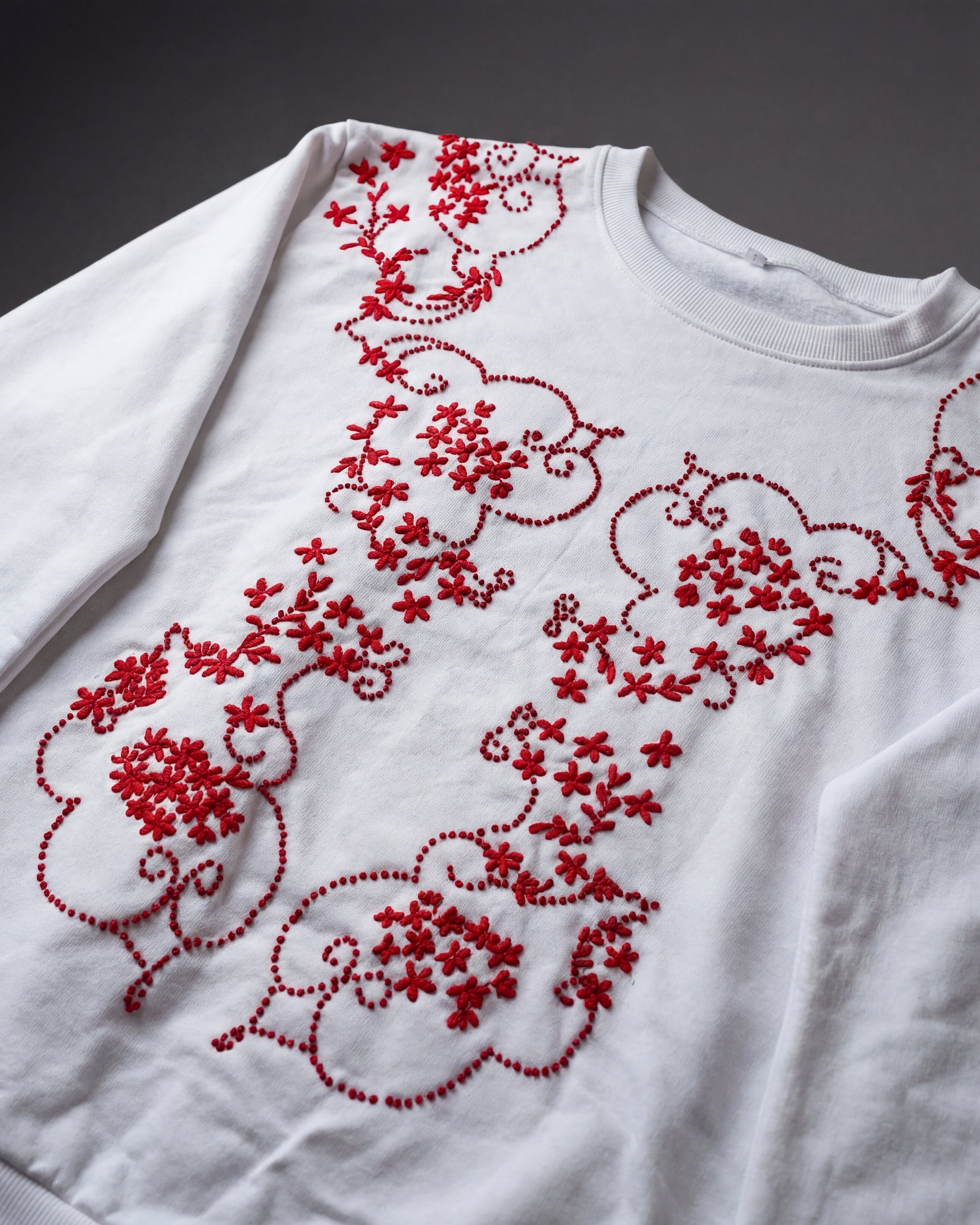 White sweatshirt with red floral embroidery on a dark background