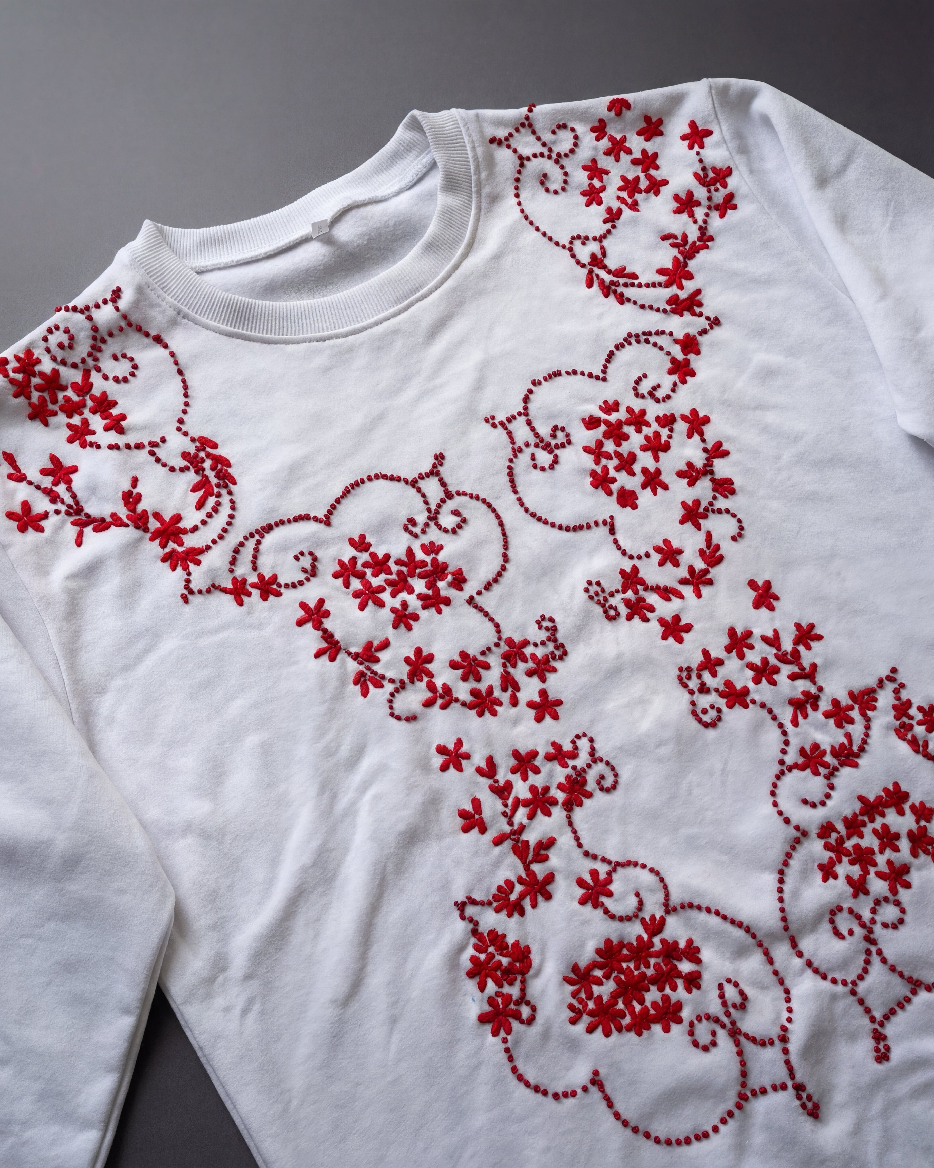 White long-sleeve shirt with red floral embroidery on a gray background