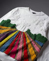 White sweater with colorful, textured embroidered design  on a dark background